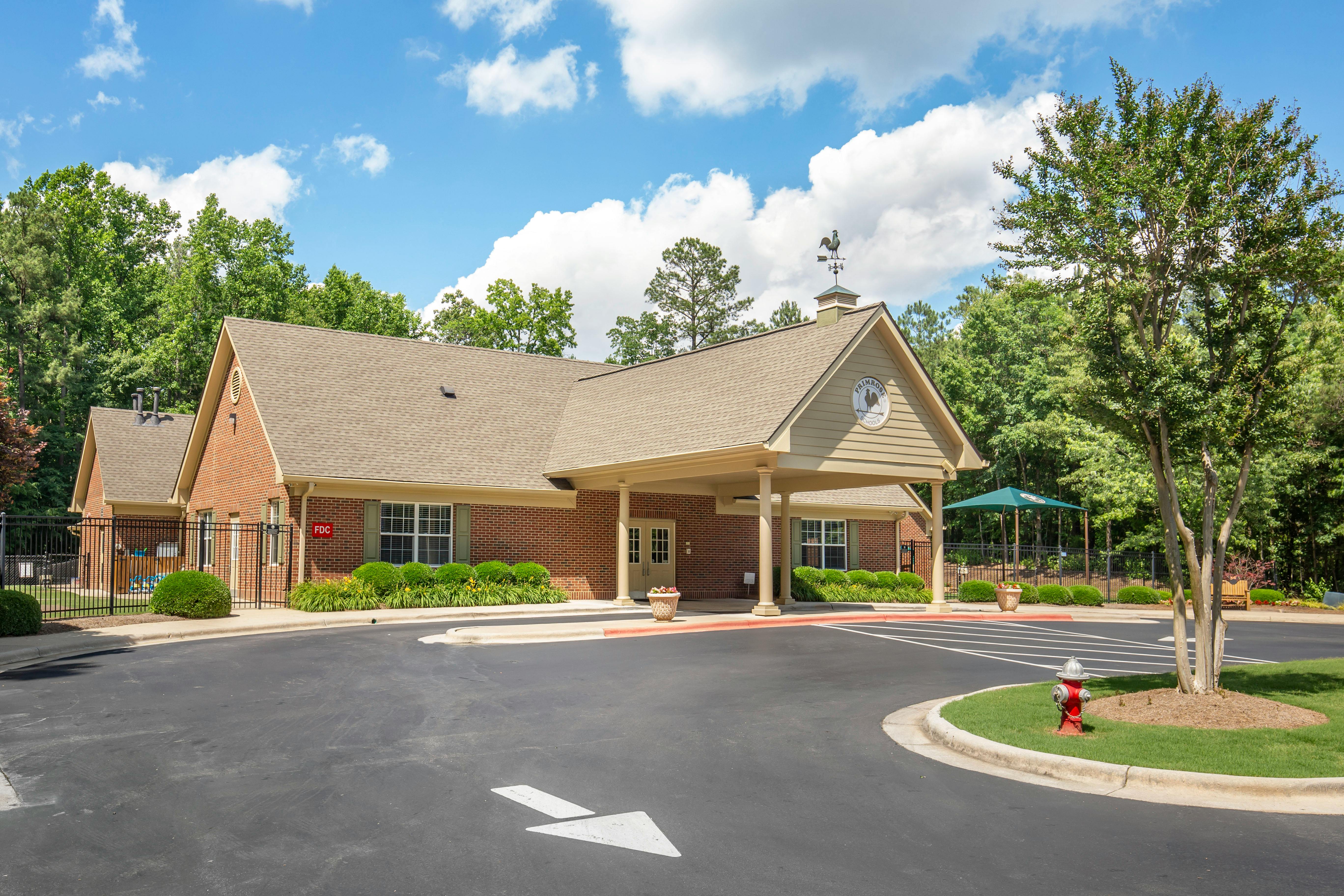 Brick building with gabled roofs and covered entrance, surrounded by trees and a parking lot