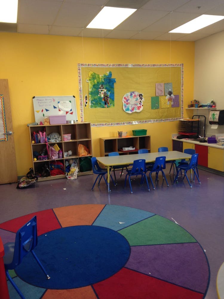 Classroom with yellow walls, tables, chairs, and a colorful rug