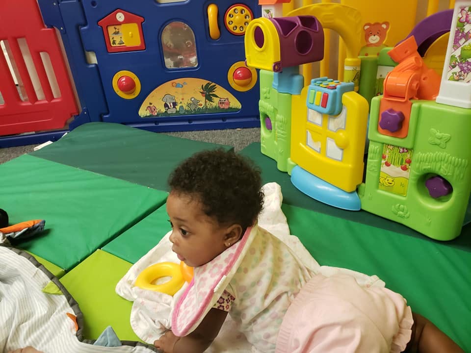 Child crawling on a green mat near colorful toys
