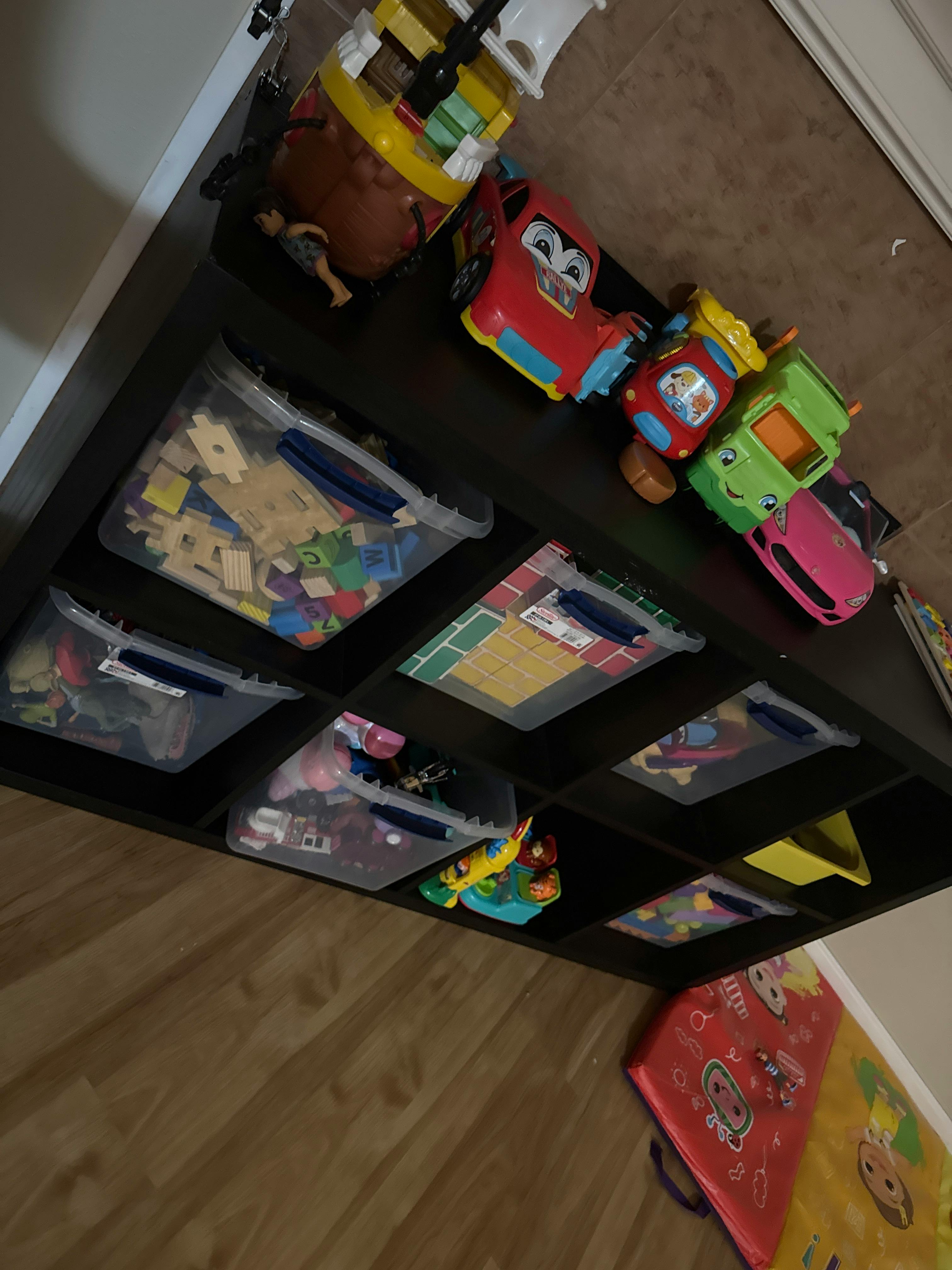 Toy storage shelf with plastic bins filled with toys and toy vehicles on top