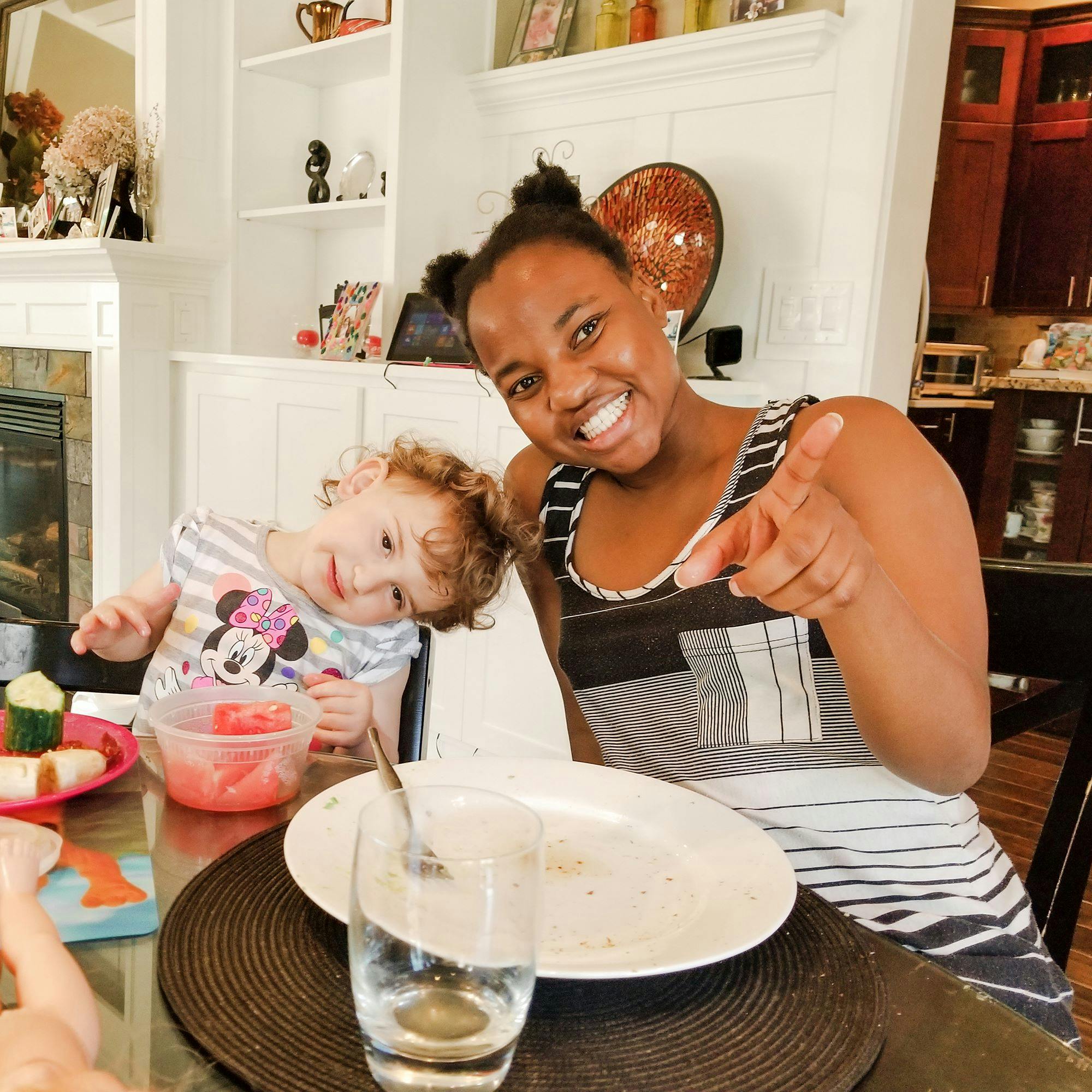 Person pointing at camera with child next to them at a table