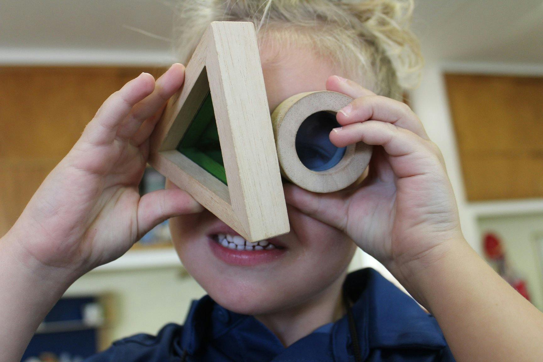 Child holding wooden shapes over eyes