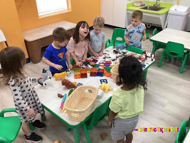 Group of children playing with toy animals and magnetic tiles on a table