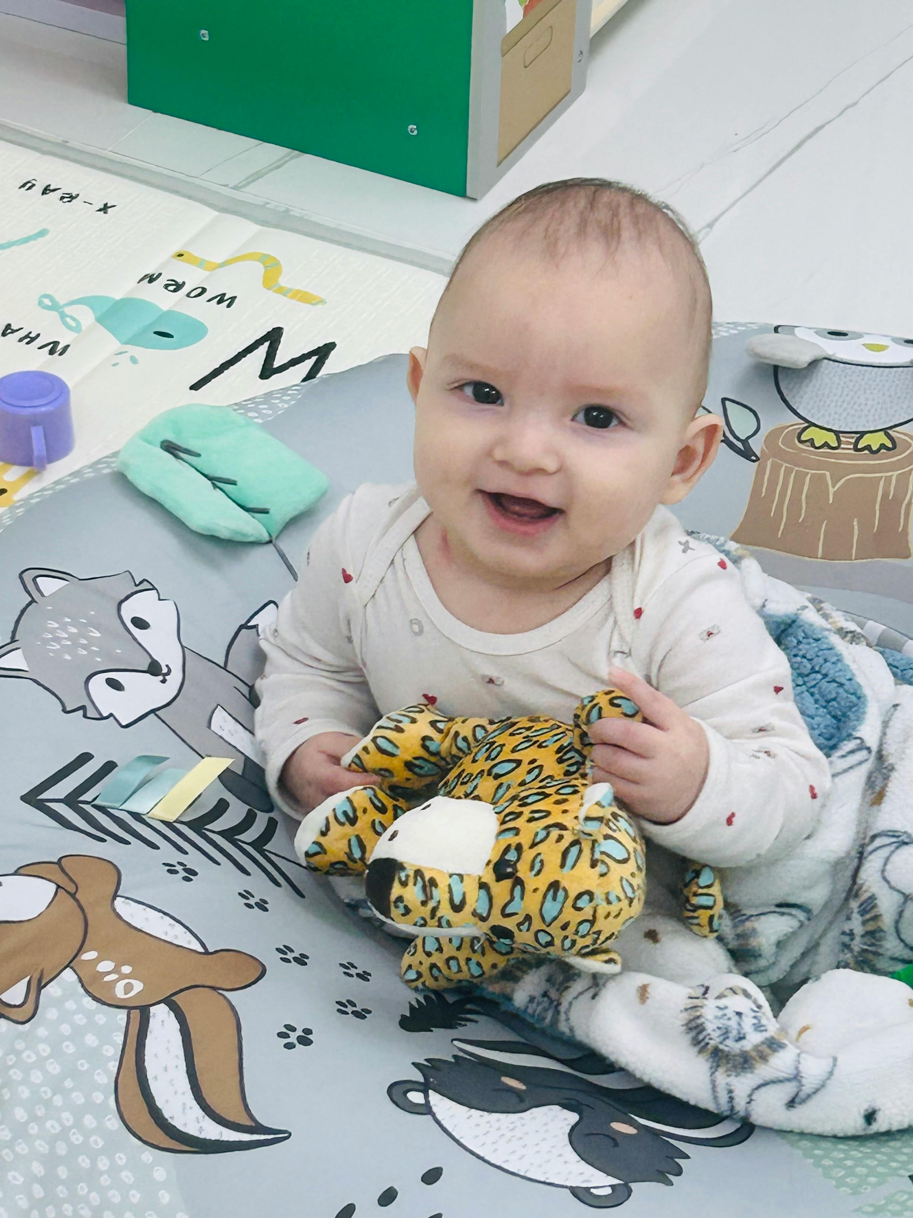 Child sitting on a playmat holding a stuffed animal