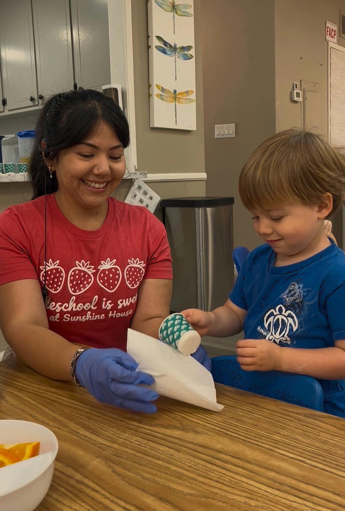 A person and a child at a table using a small cup and paper napkin