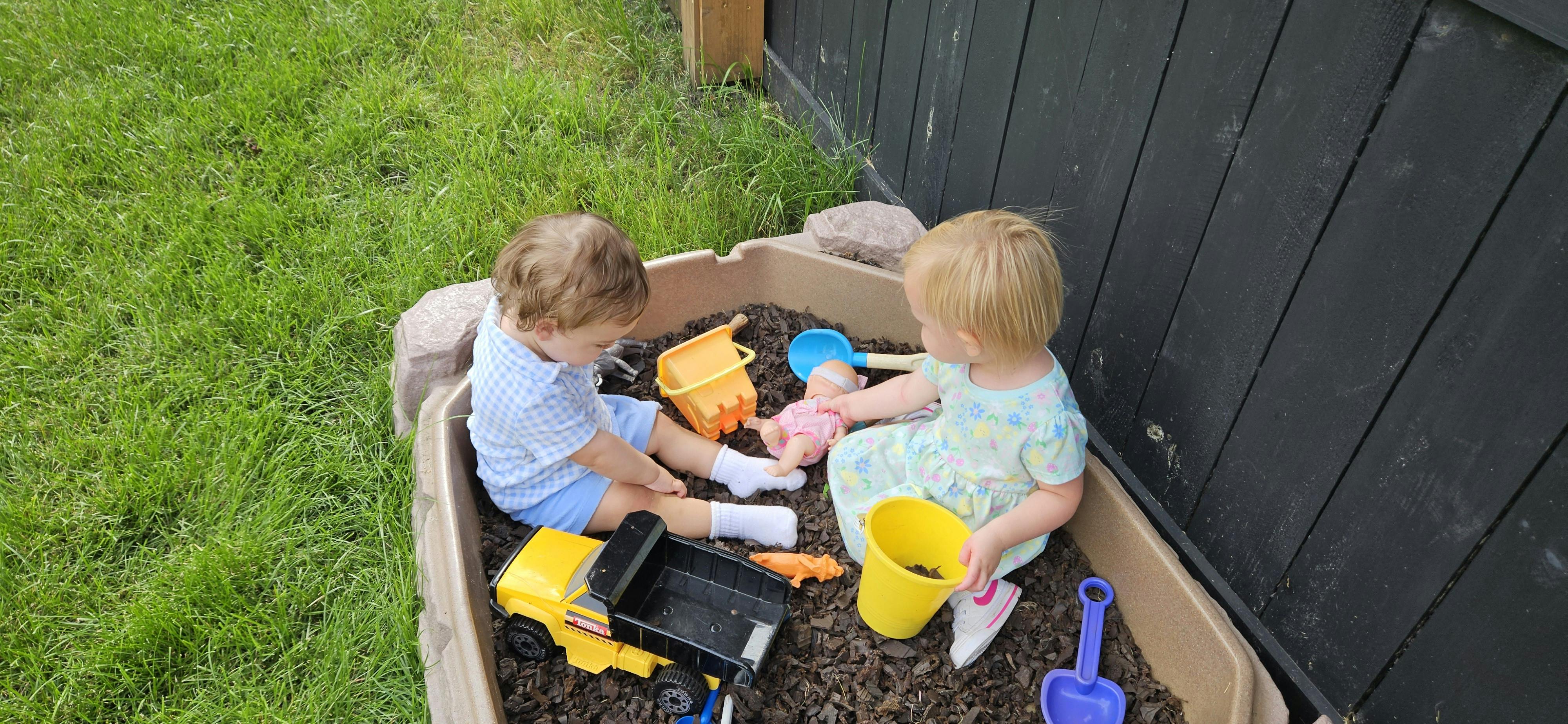 Two children playing in a sandbox with toys