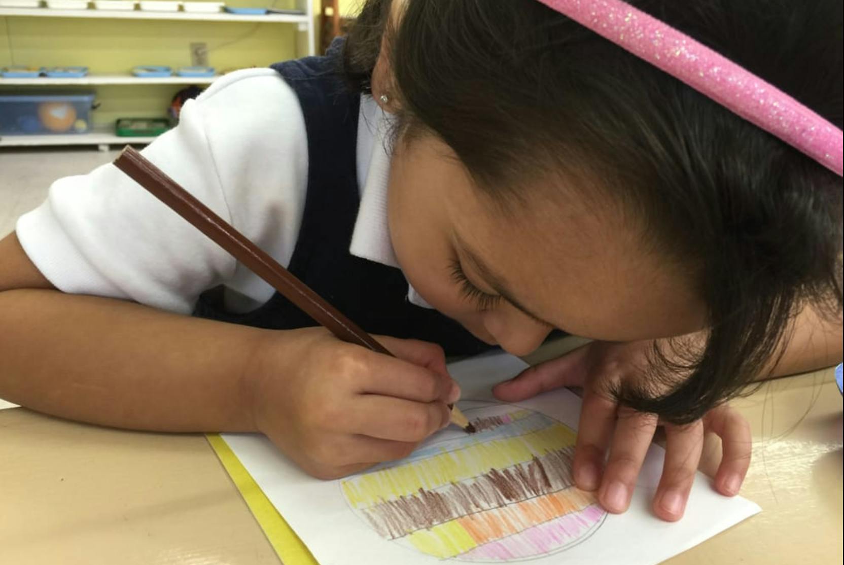 Child drawing on paper with a colored pencil