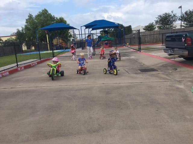 Children riding tricycles on pavement near a playground