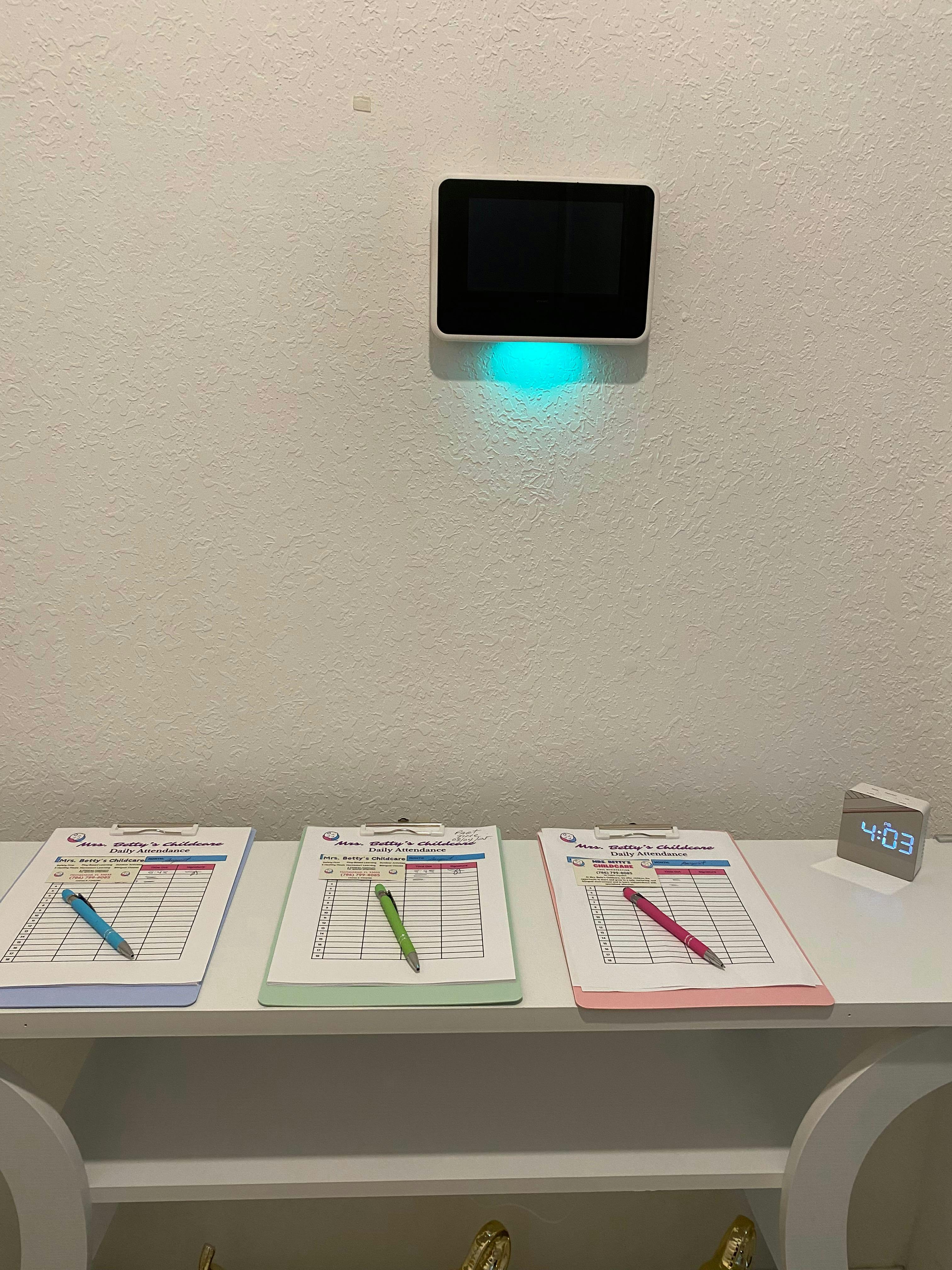 Three clipboards with pens on a shelf below a wall-mounted screen