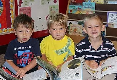 Three children sitting with open books in a classroom