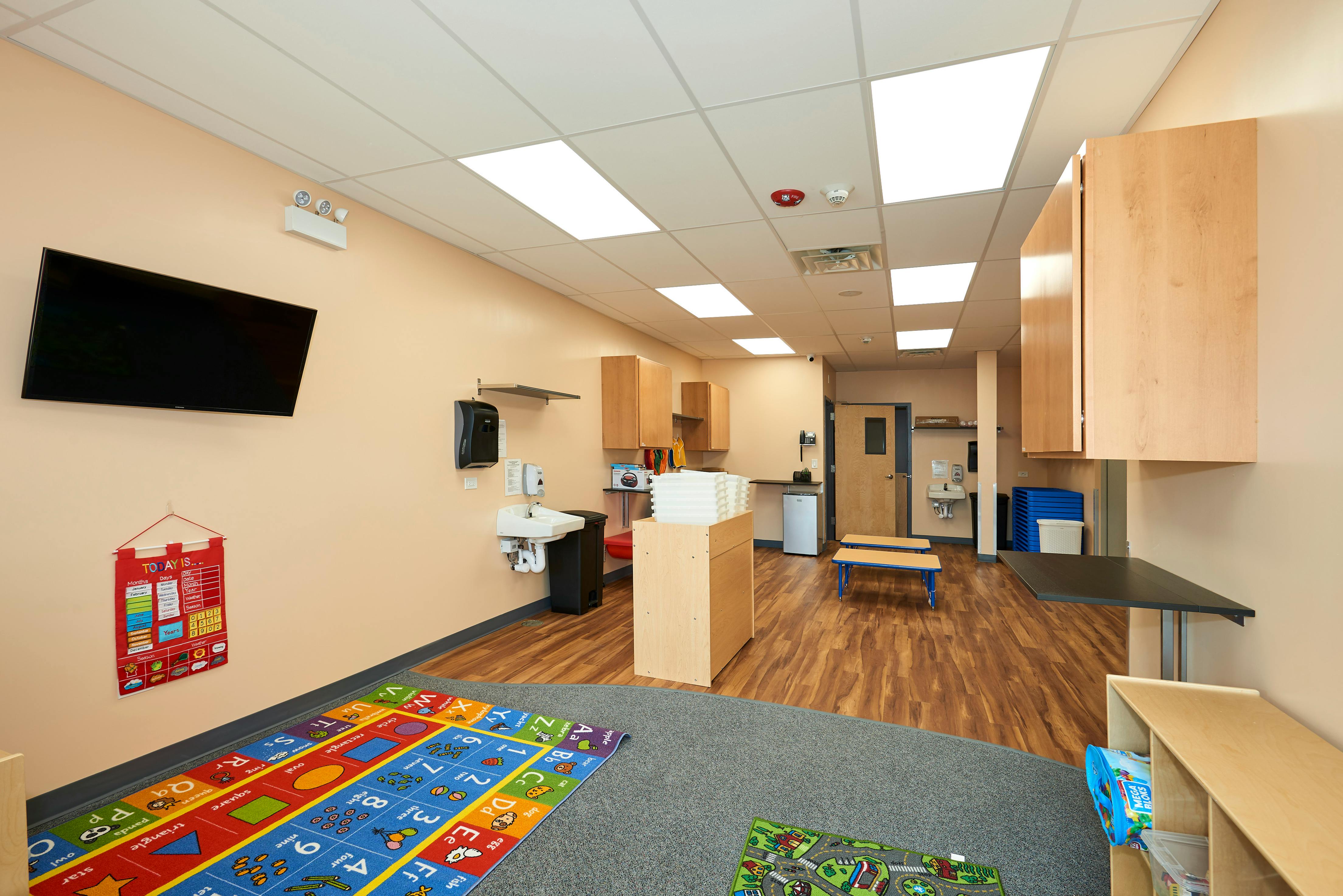 Classroom with a TV, sink, and play rugs