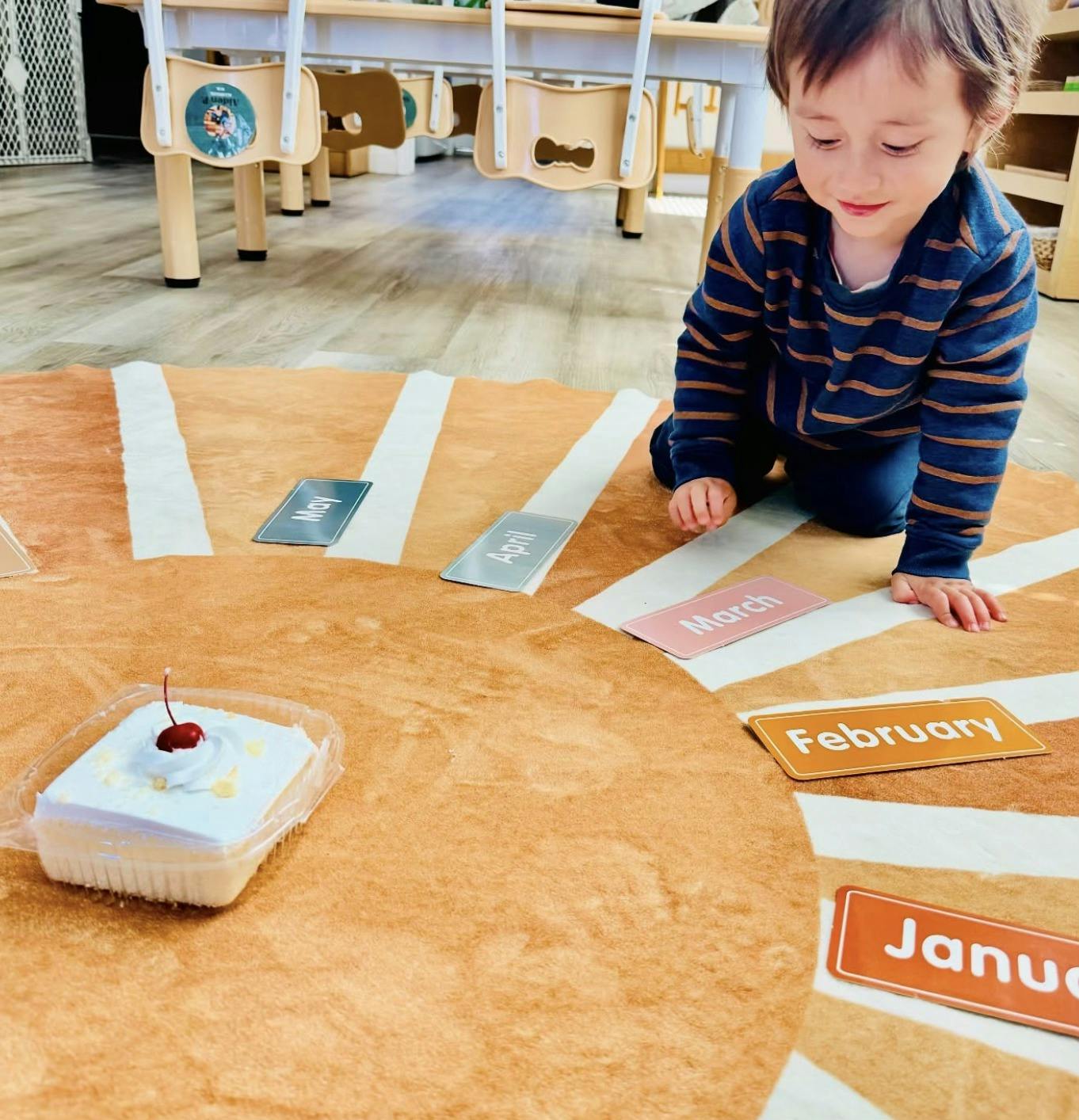 Child kneeling on a rug with cards, looking at a small cake