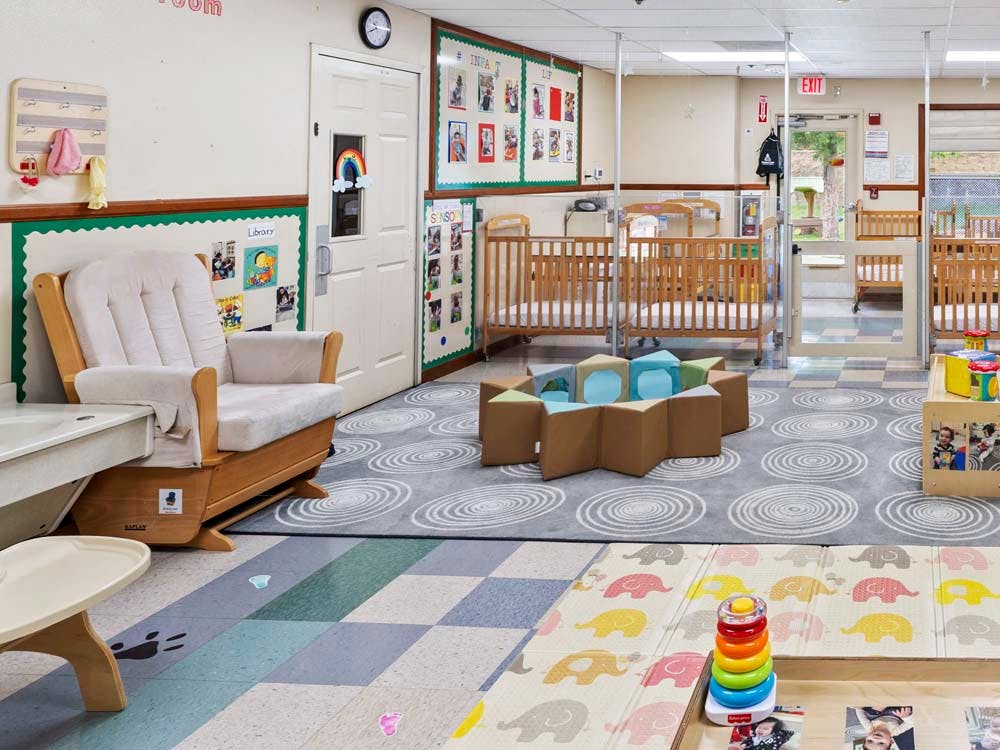 cribs in a daycare room with a rocking chair and play area