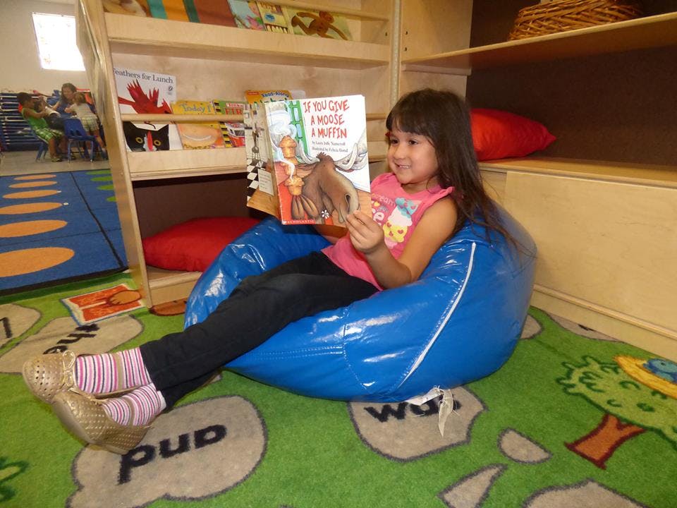 Child sitting in a blue beanbag chair reading a book