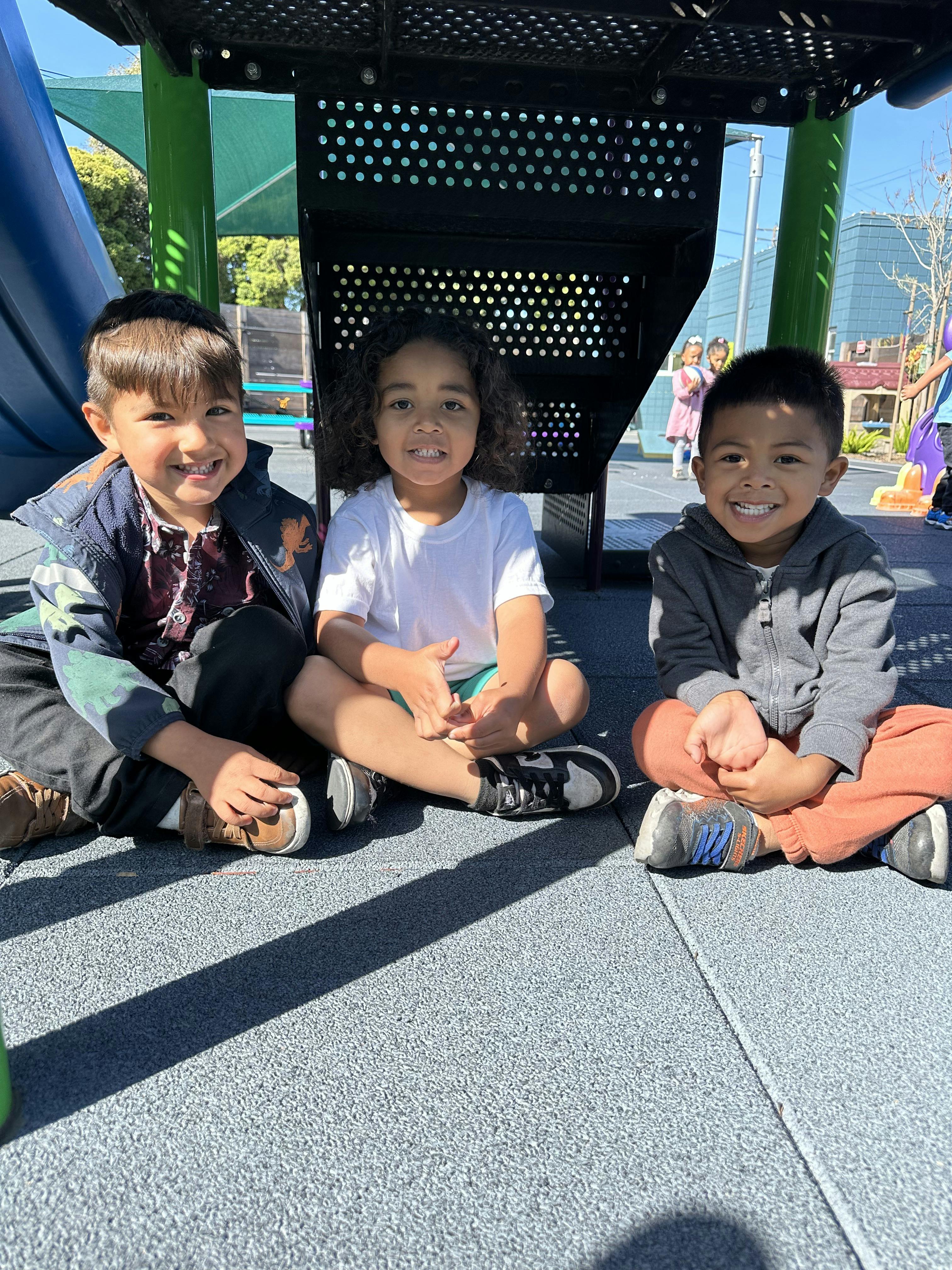 Three children sitting on the ground at a playground