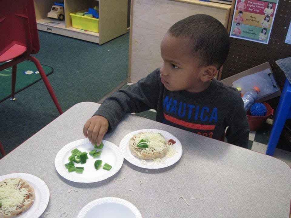 Child adding green peppers to a small pizza
