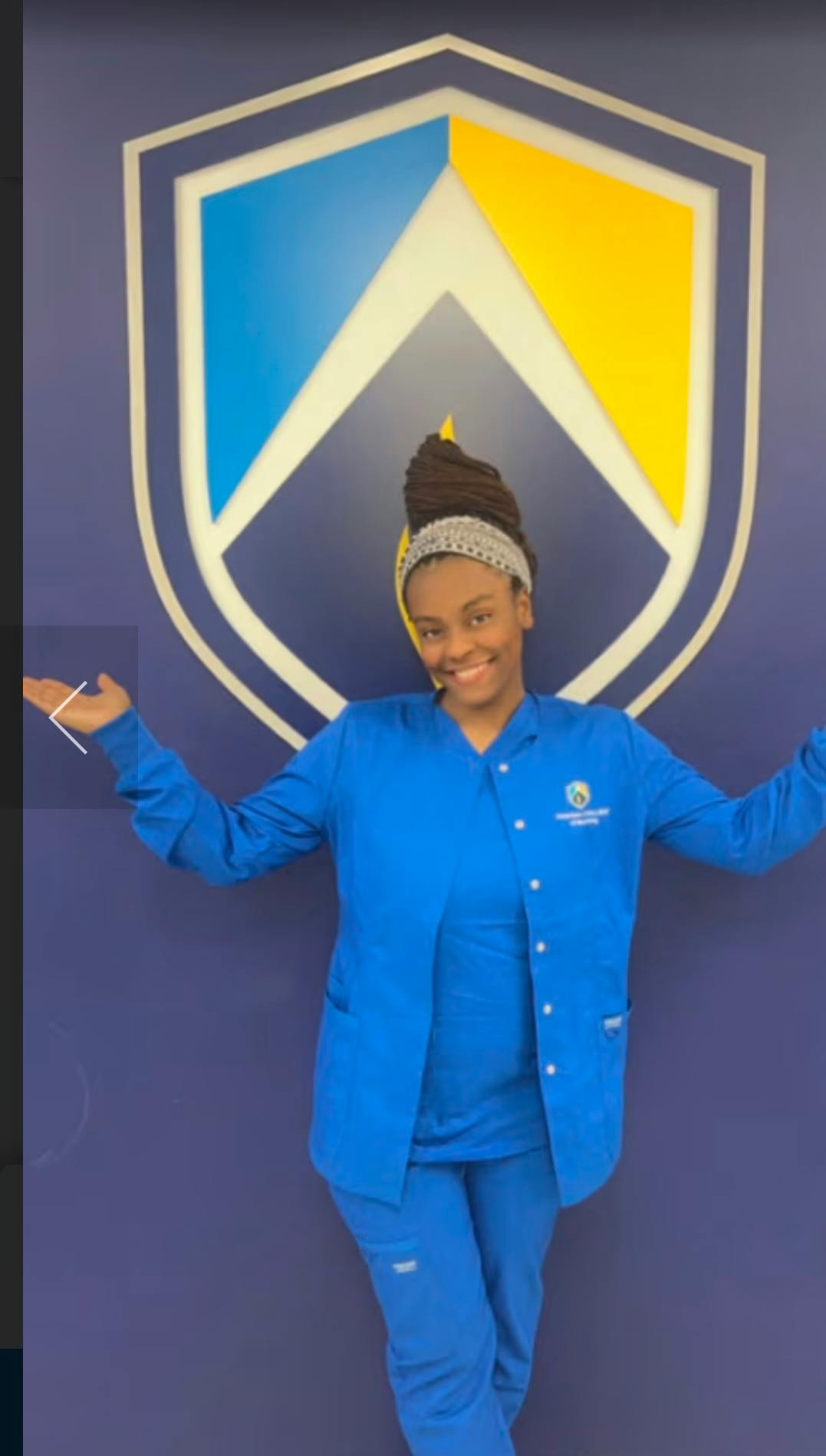 Person in blue scrubs standing in front of a shield logo