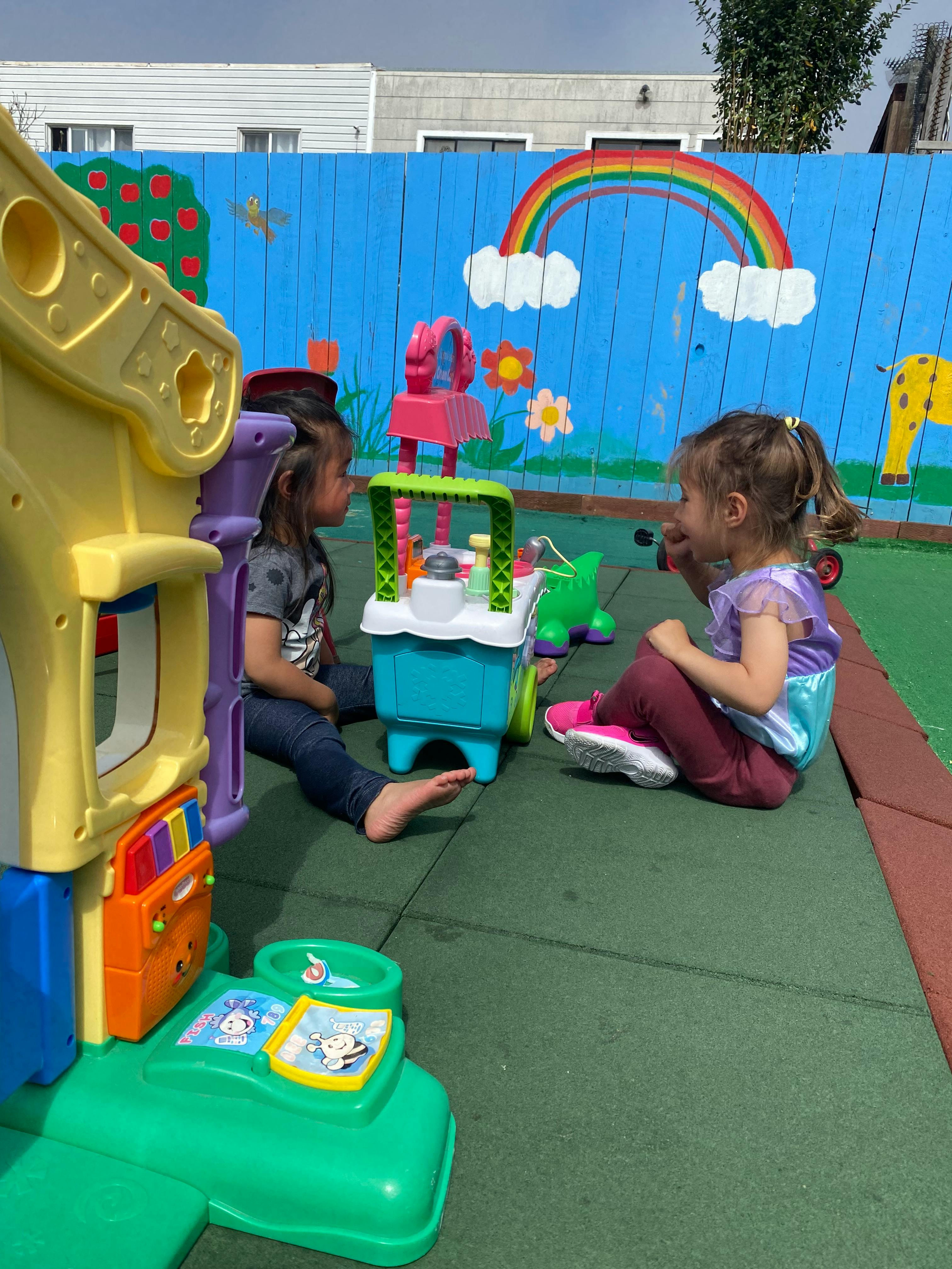 Two children playing with toys on a green mat outdoors