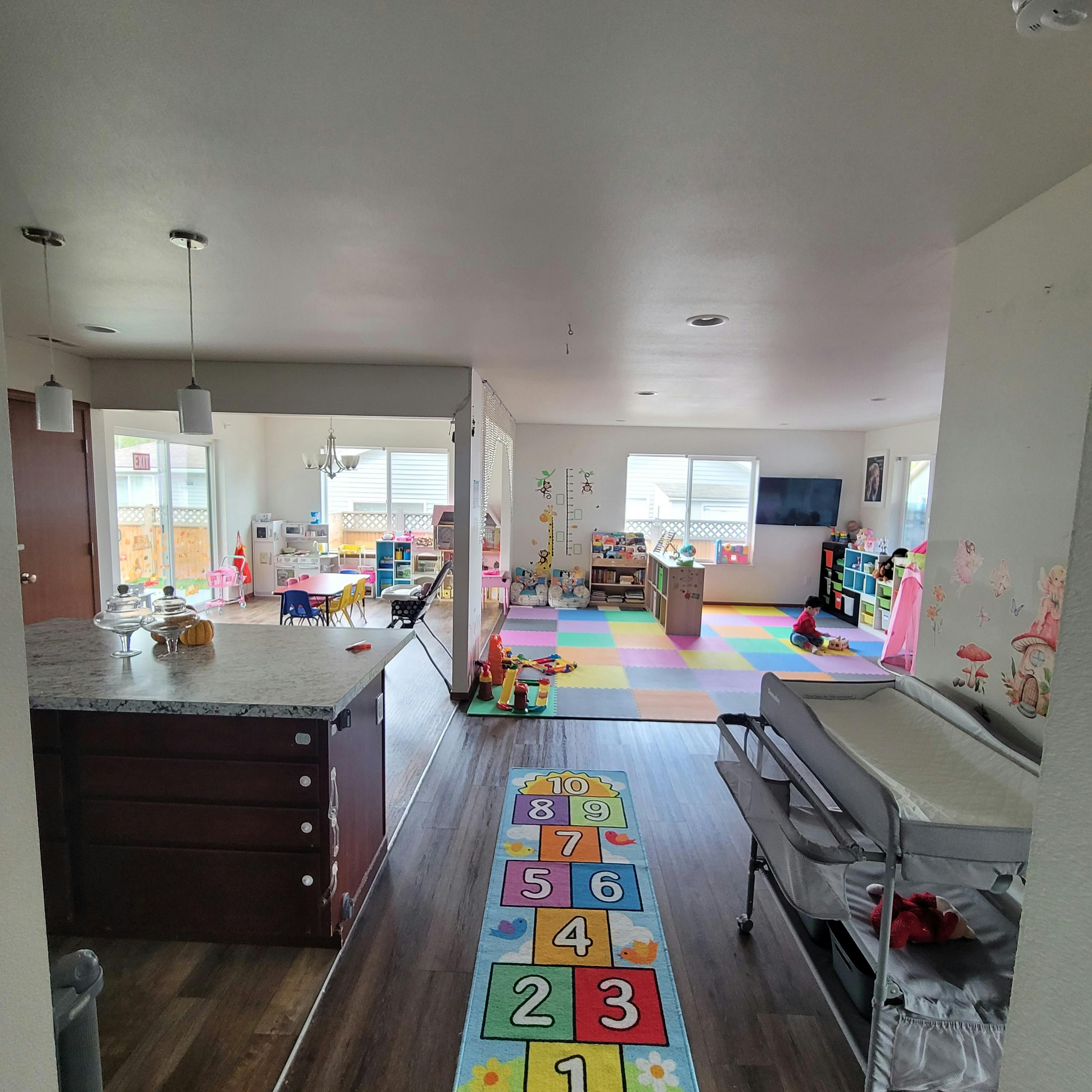 Playroom with colorful floor mats and toys, next to a kitchen island