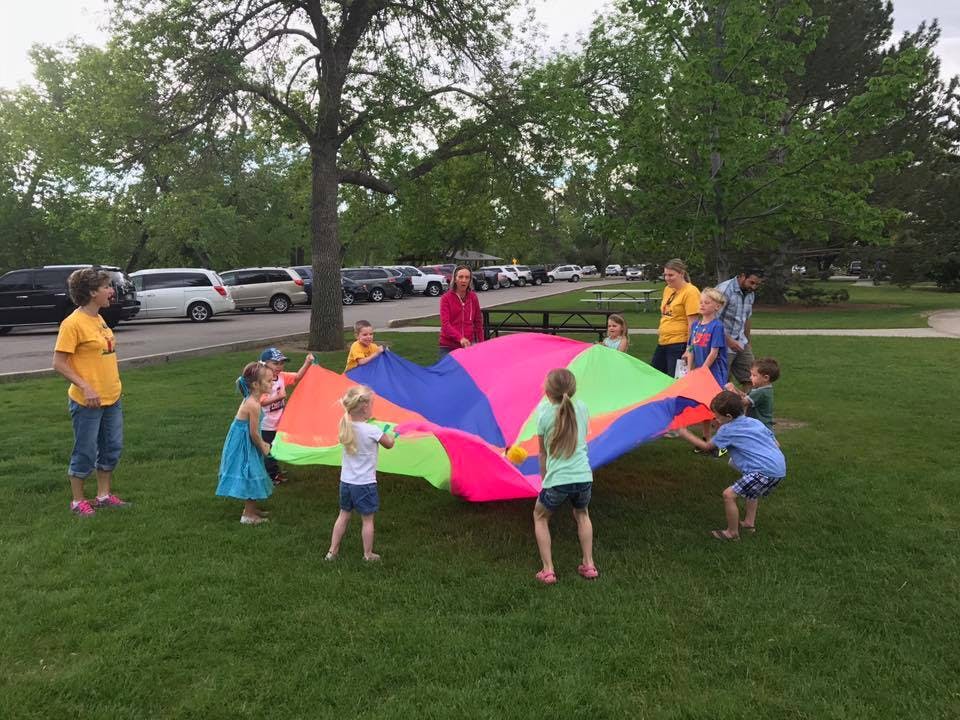 Adults and children playing with a colorful parachute on grass