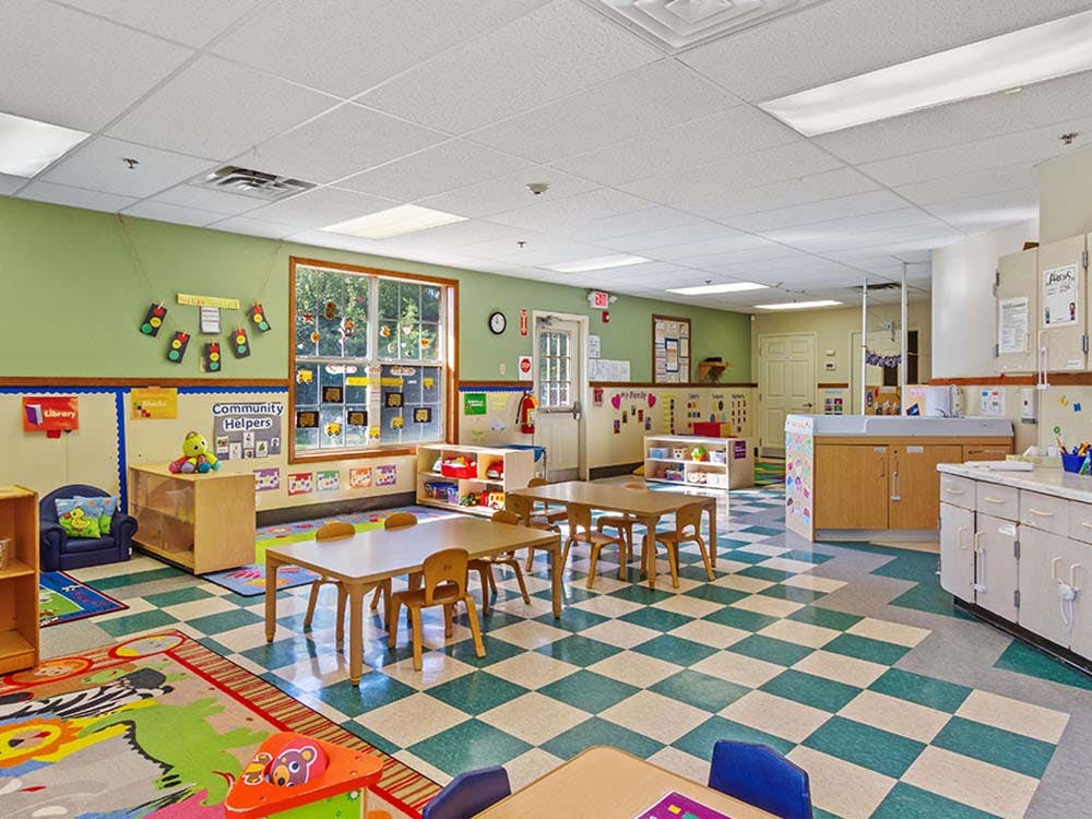 Child care classroom with small tables and chairs, colorful rugs, and a large window