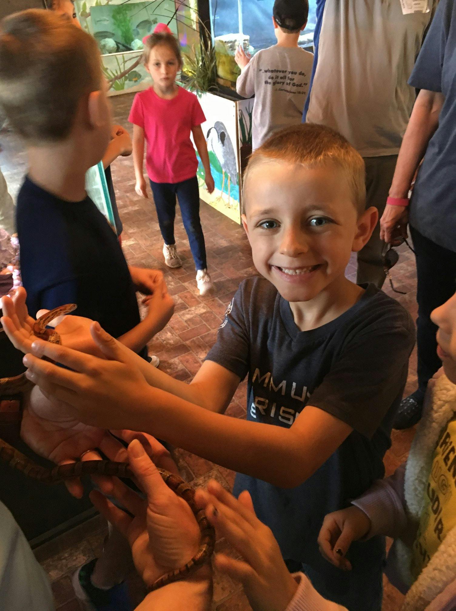 Child holding a snake with other children in the background