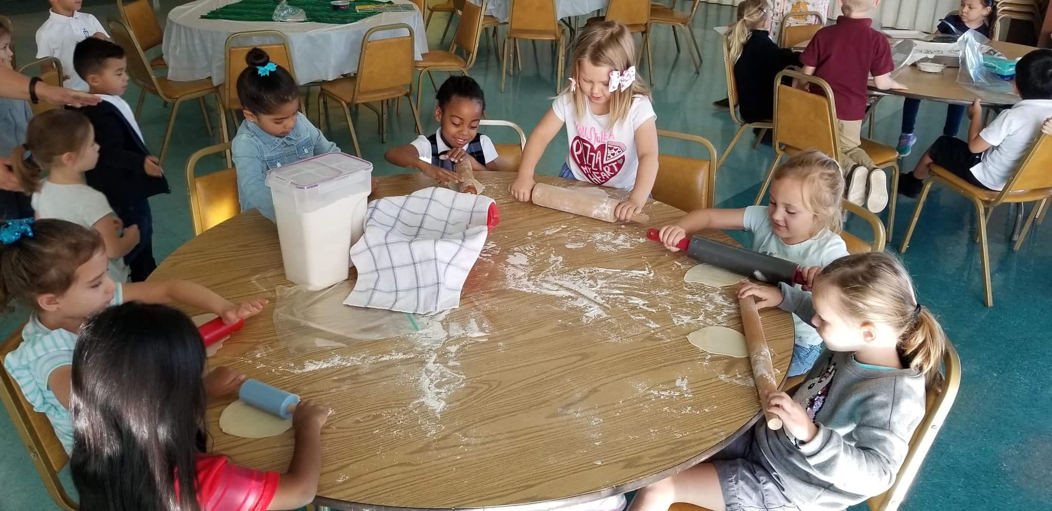 Children around a table with flour and rolling pins