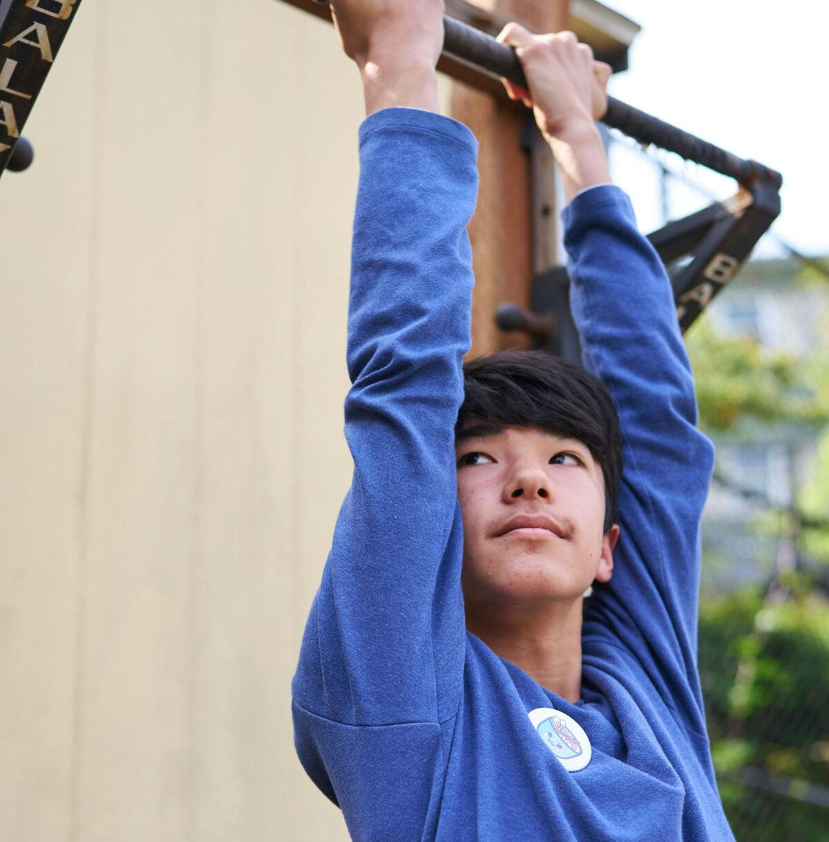 Child hanging from a horizontal bar outdoors, looking up and to the right