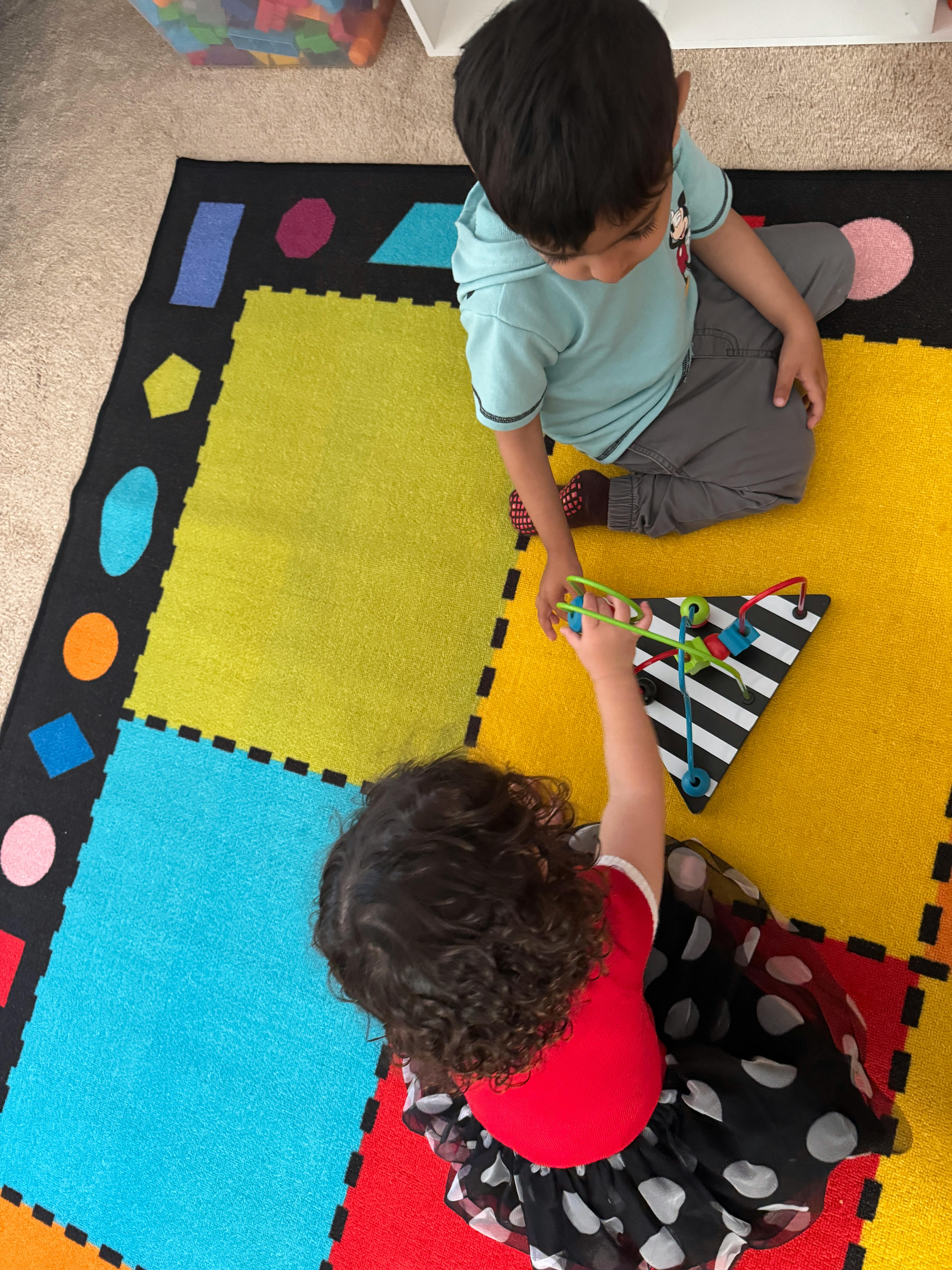 Two children playing with a toy on a colorful mat