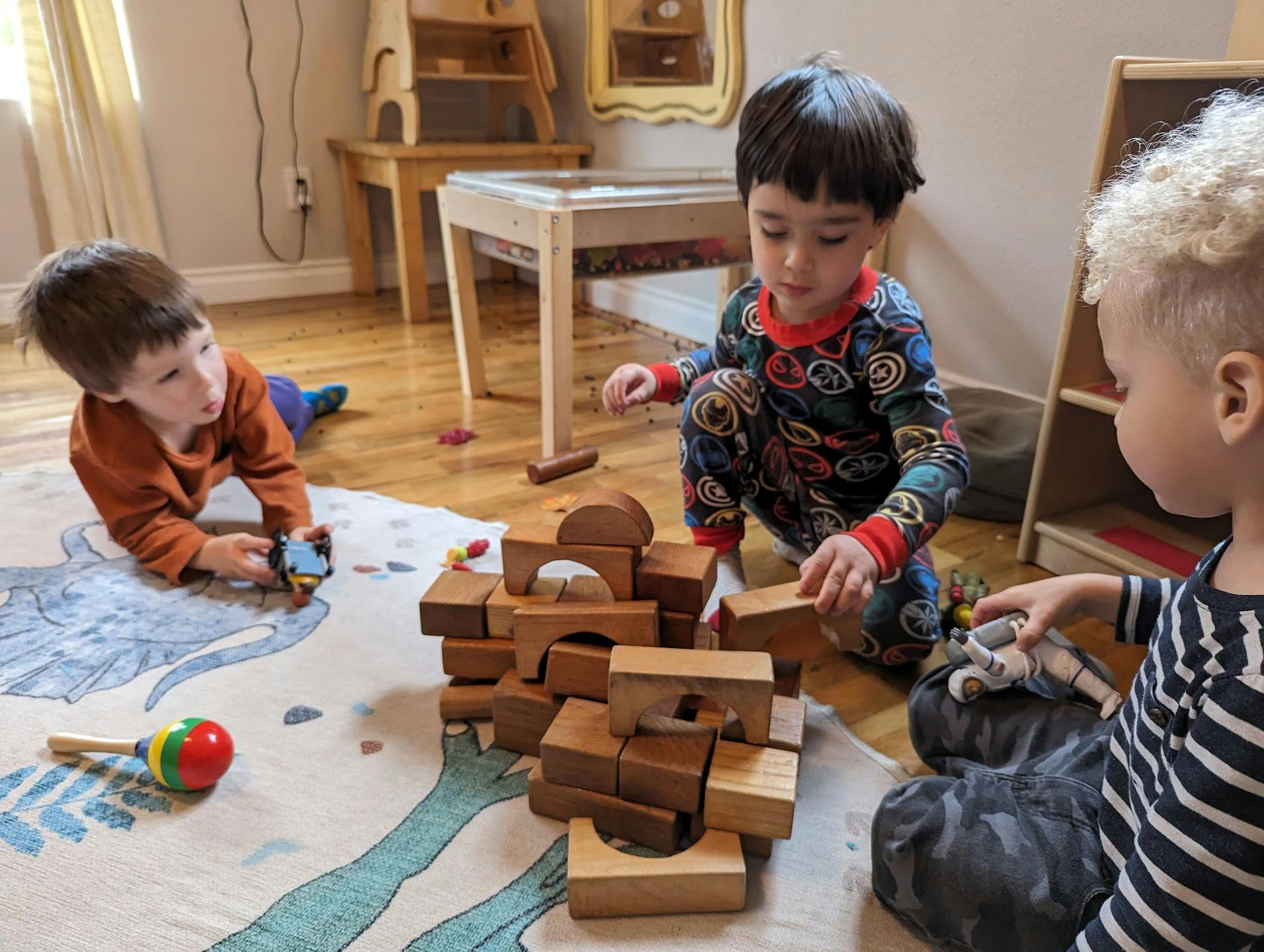 Three children playing with wooden blocks on a rug