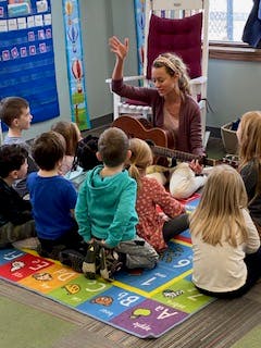 Adult playing guitar and singing to a group of children
