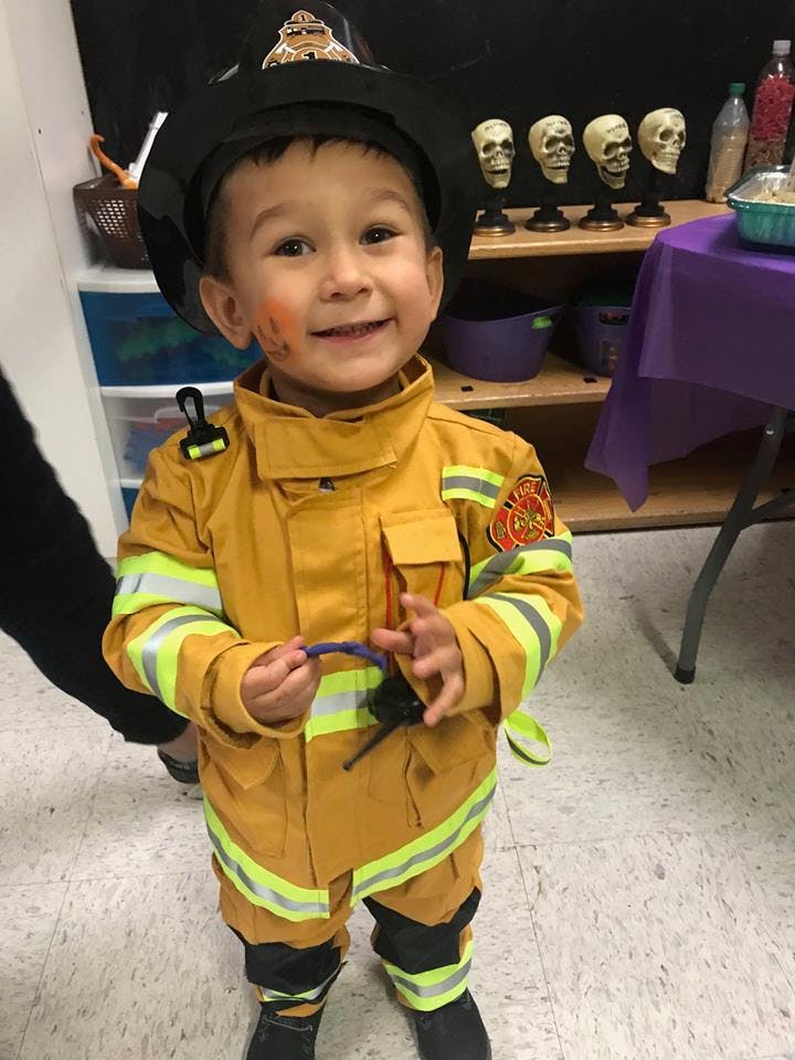 Child in a firefighter costume holding a toy radio