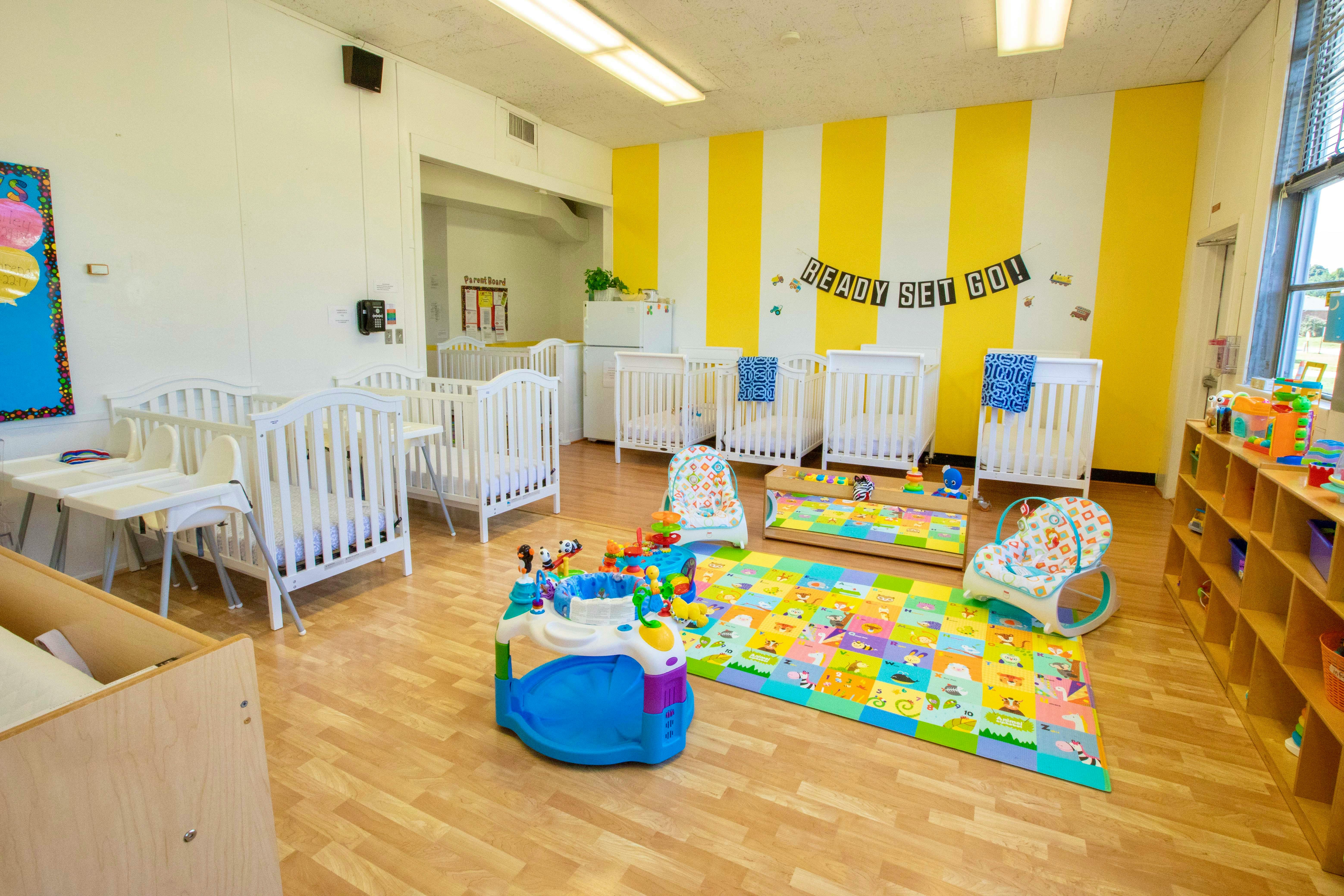 Nursery room with multiple cribs, playmat, and toys