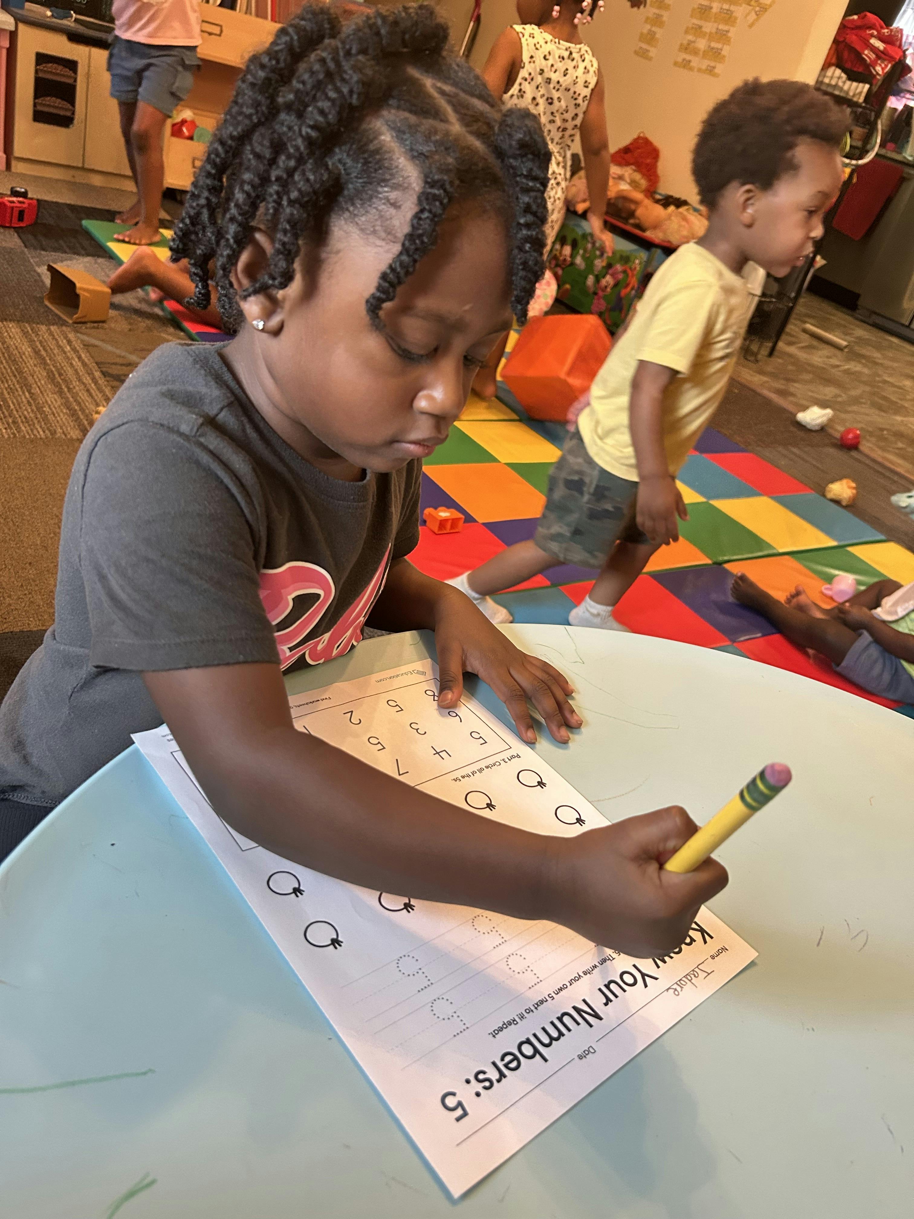 Child writing on a number worksheet at a table in a classroom