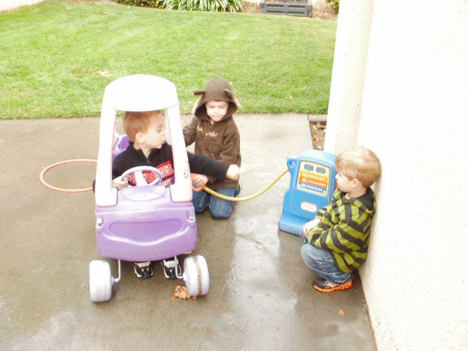 Three children playing with a toy car and gas pump