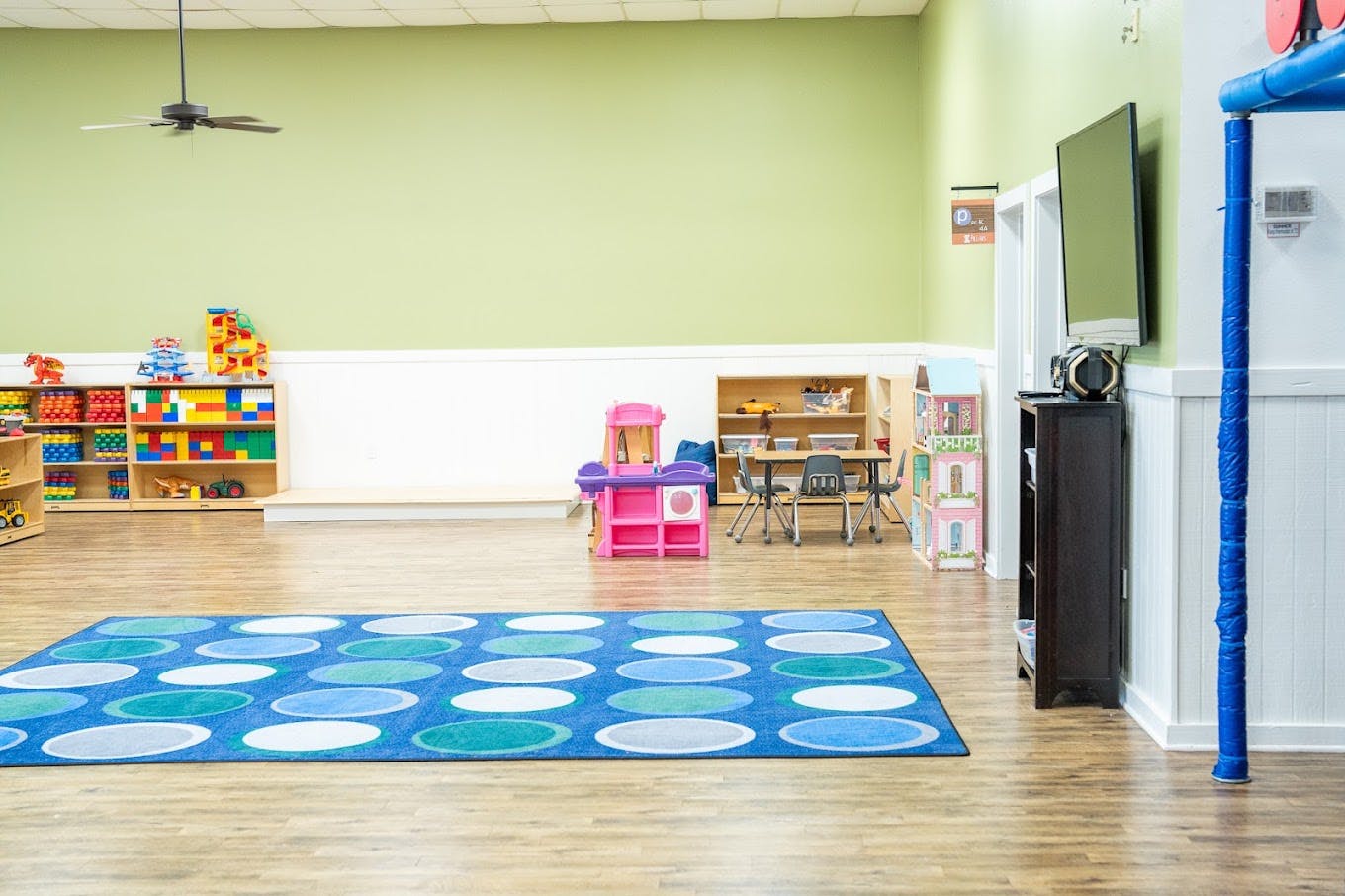 Colorful playroom with shelves of toys, a small table, and patterned area rug
