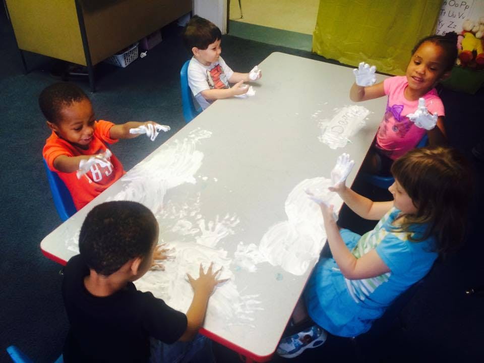 Children making handprints with white paint on a table