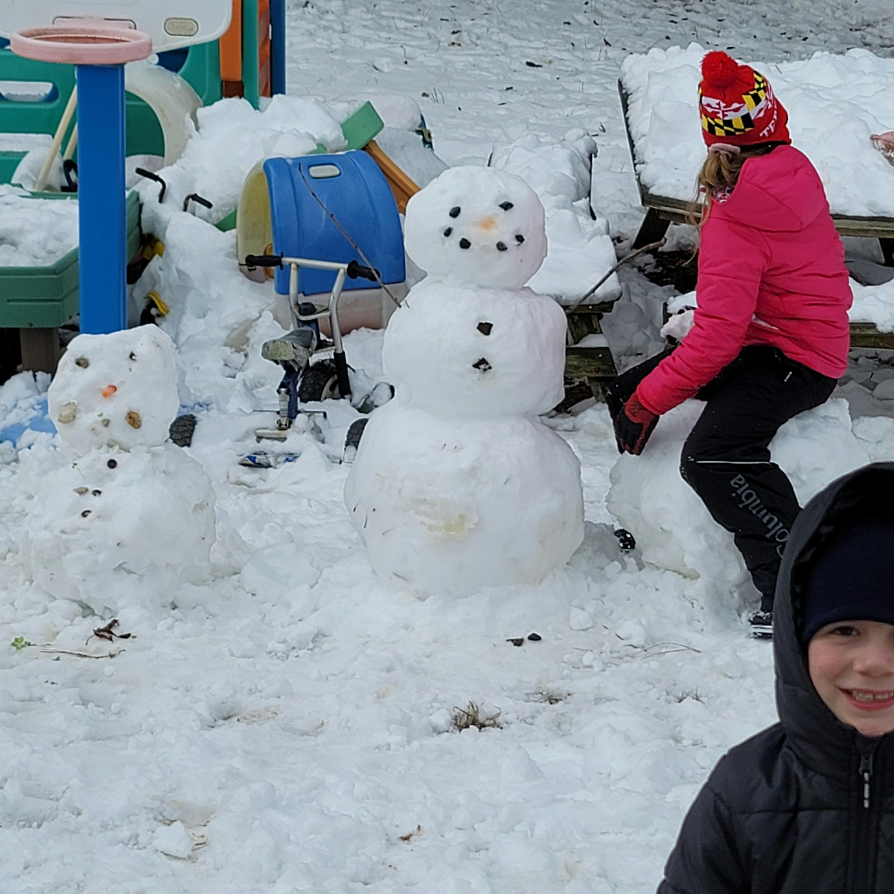 Person building a snowman next to a completed snowman