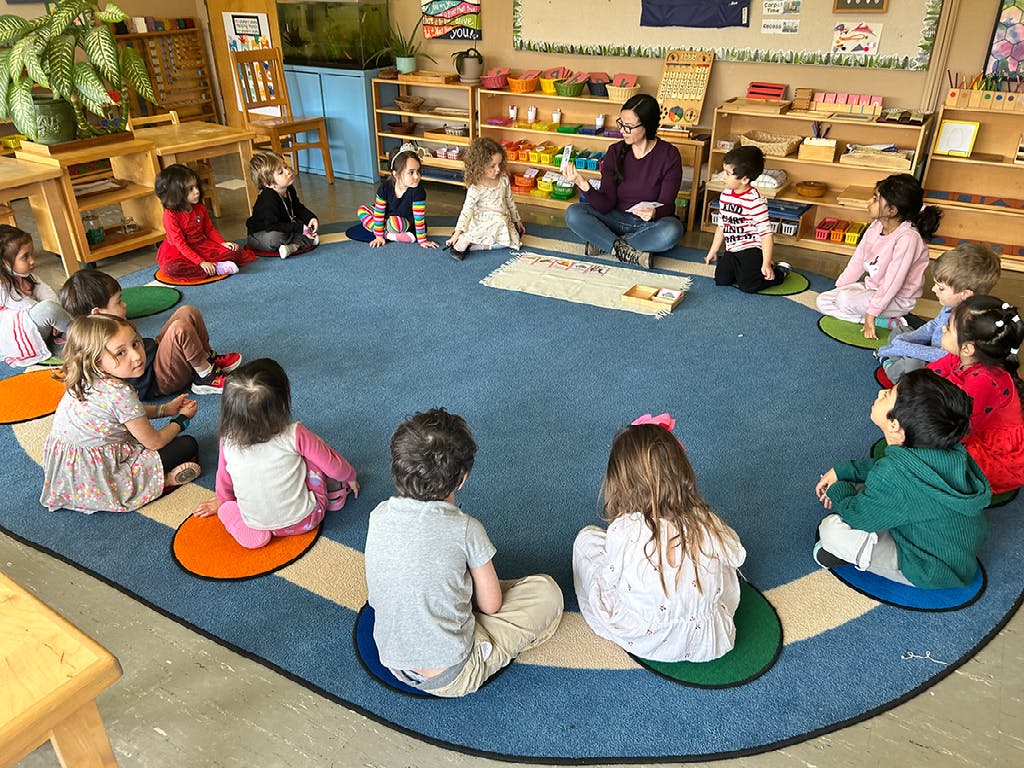 Adult and children sitting in a circle on a blue rug in a classroom