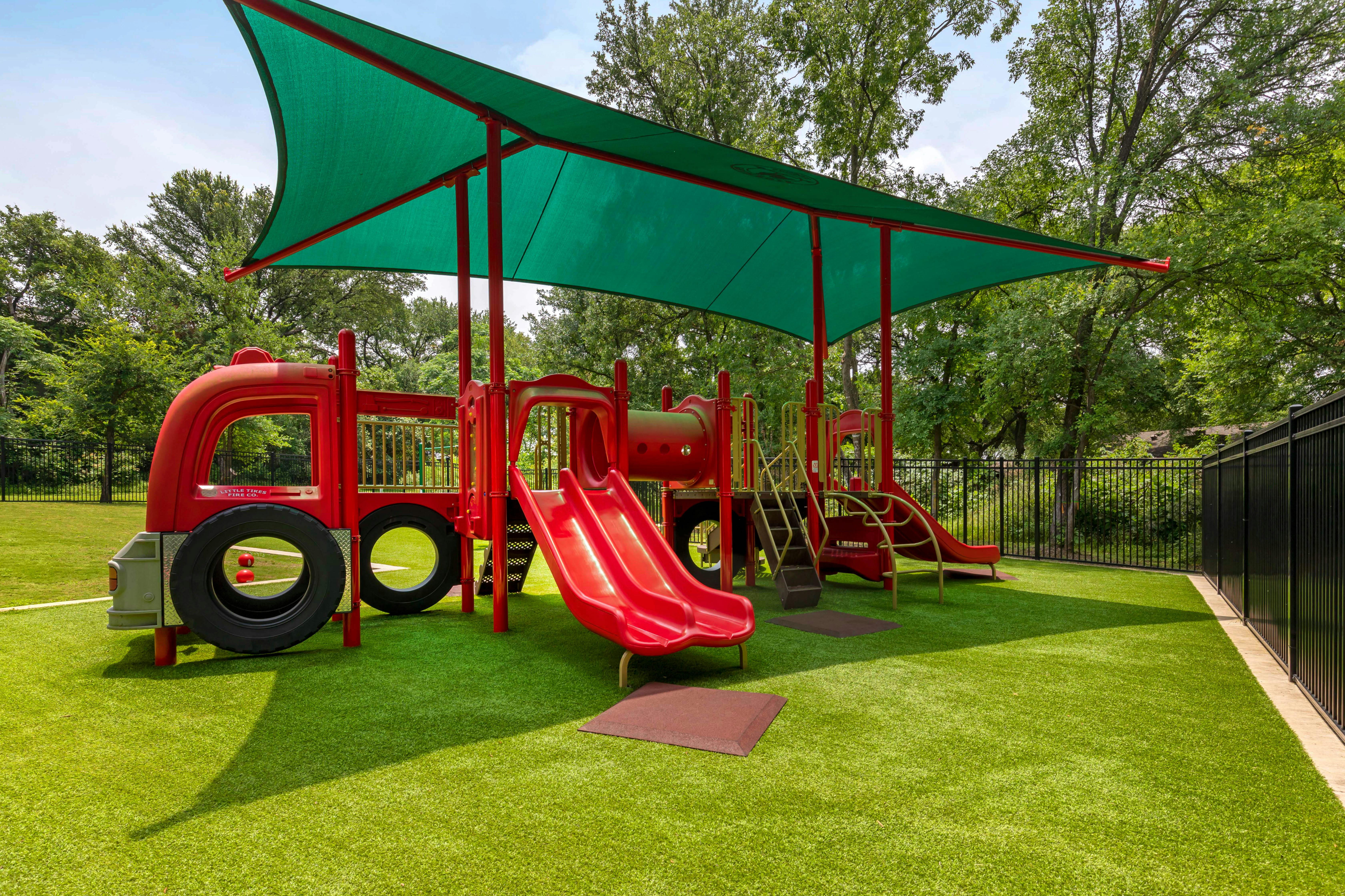 red playground structure with slides and climbing areas on green artificial turf