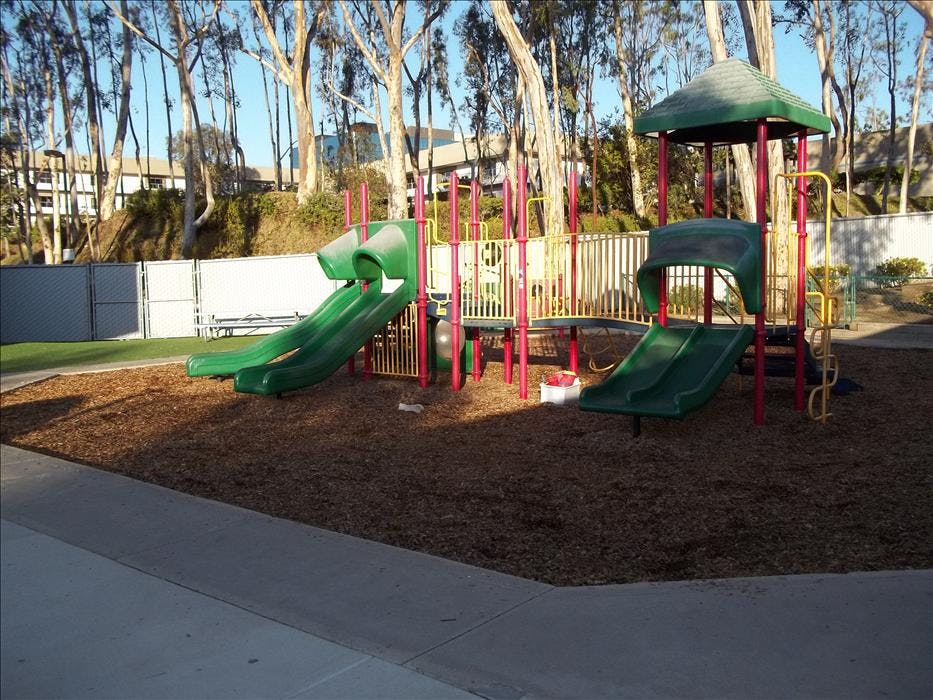 A playground with green slides, yellow and red climbing structures, and wood chips