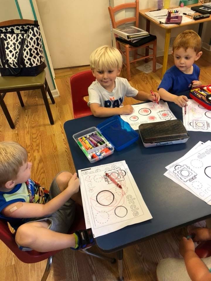 Three children coloring at a table in a classroom