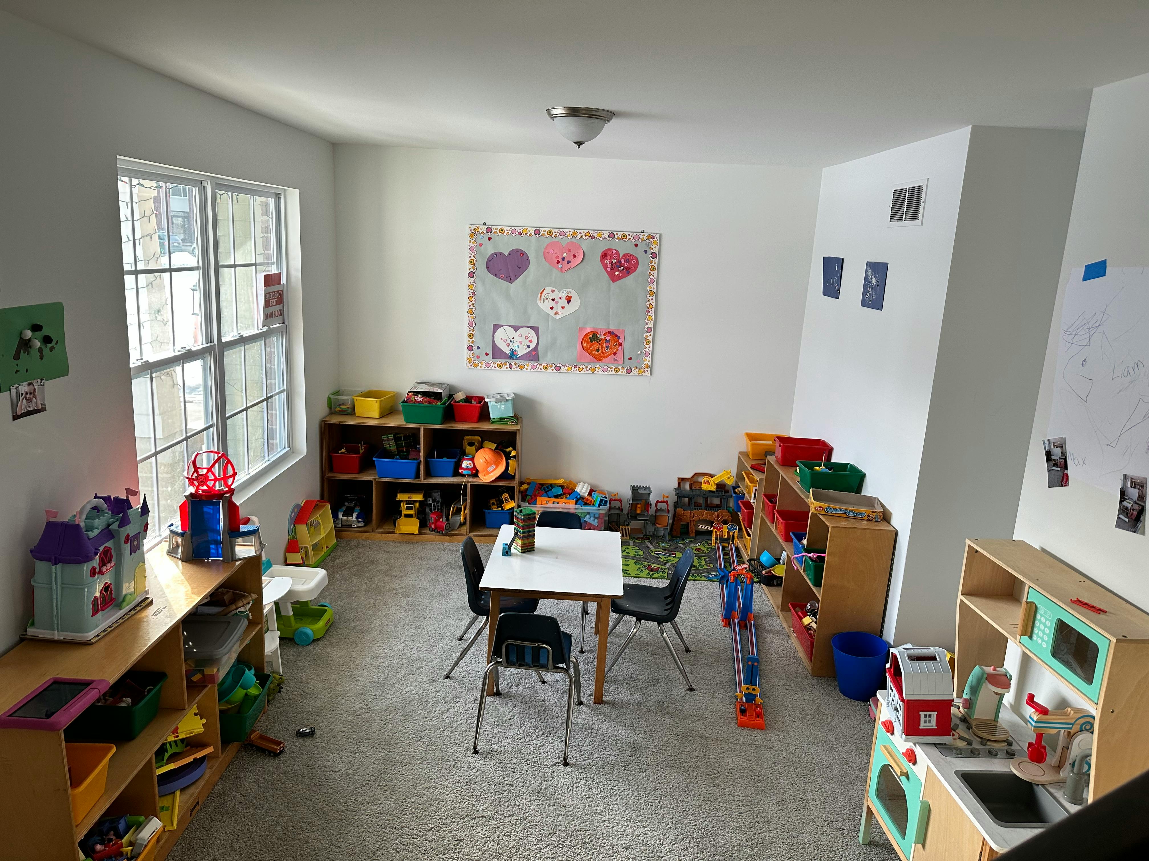 Playroom with small table and chairs, shelves with toys, and window