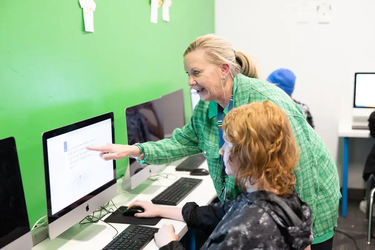 Adult pointing at a computer screen while a teen uses the mouse