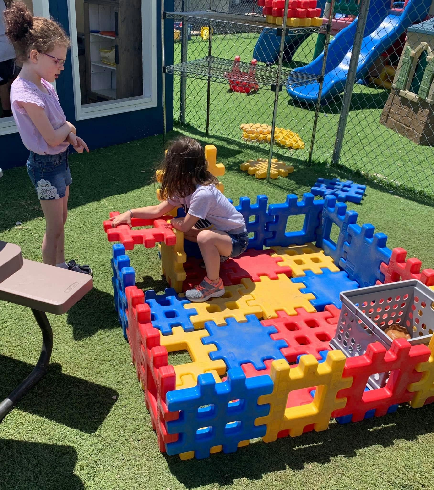 Two children playing with large colorful interlocking blocks outdoors