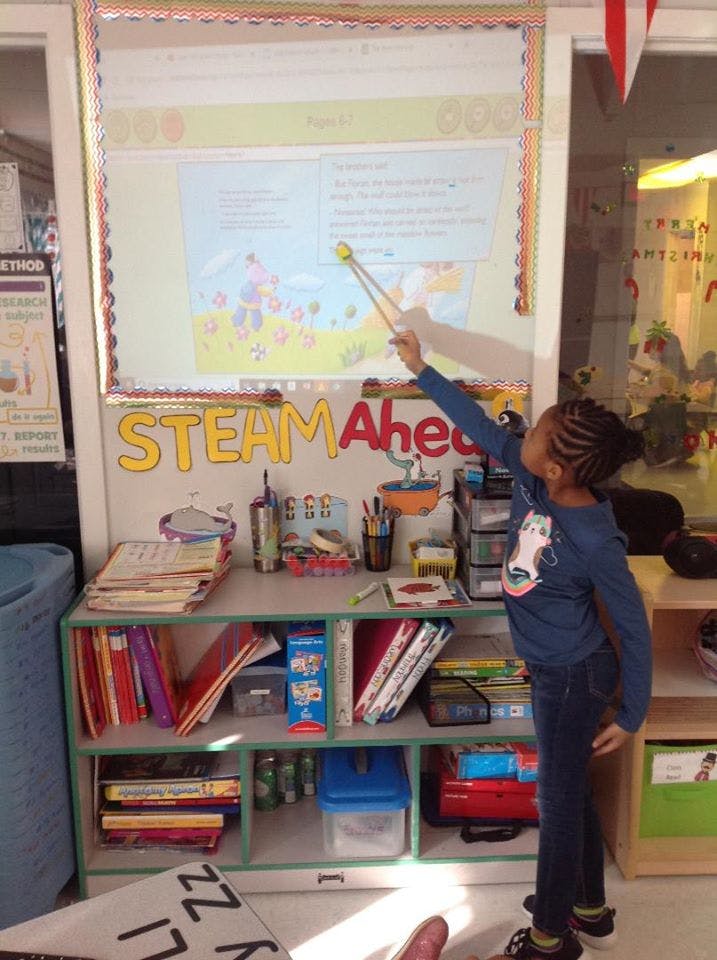 Child pointing a stick at a projected image on a classroom wall