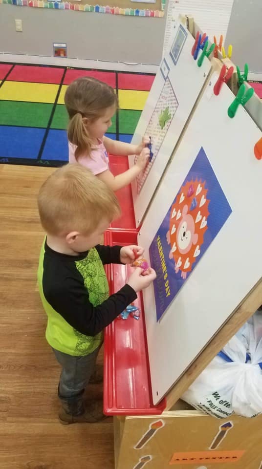 Two children playing at an easel in a classroom