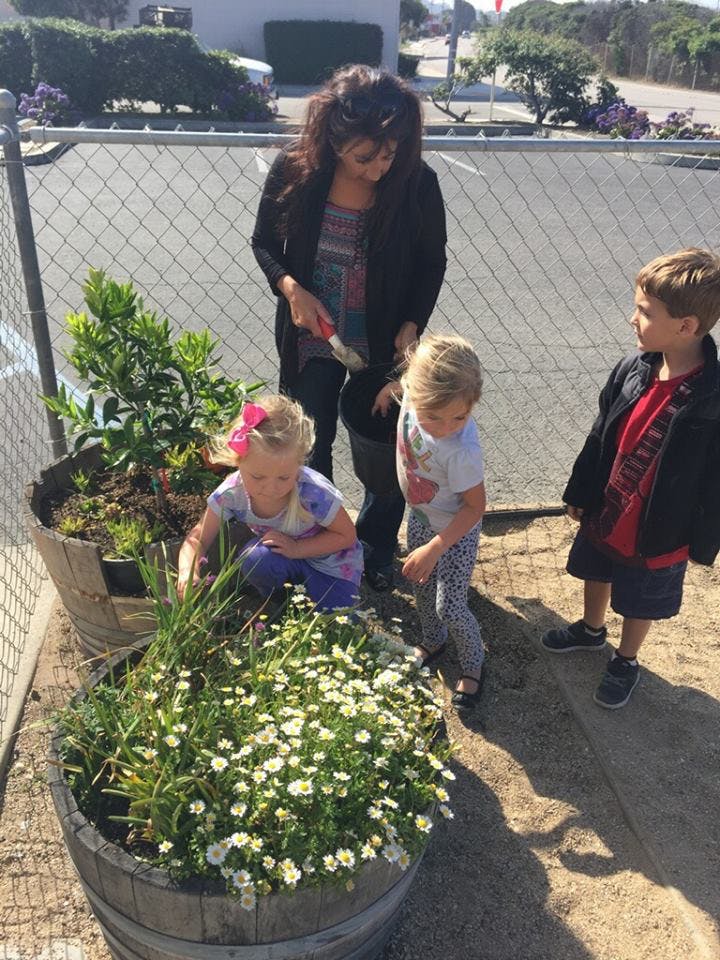 Person and three children gardening in large planters