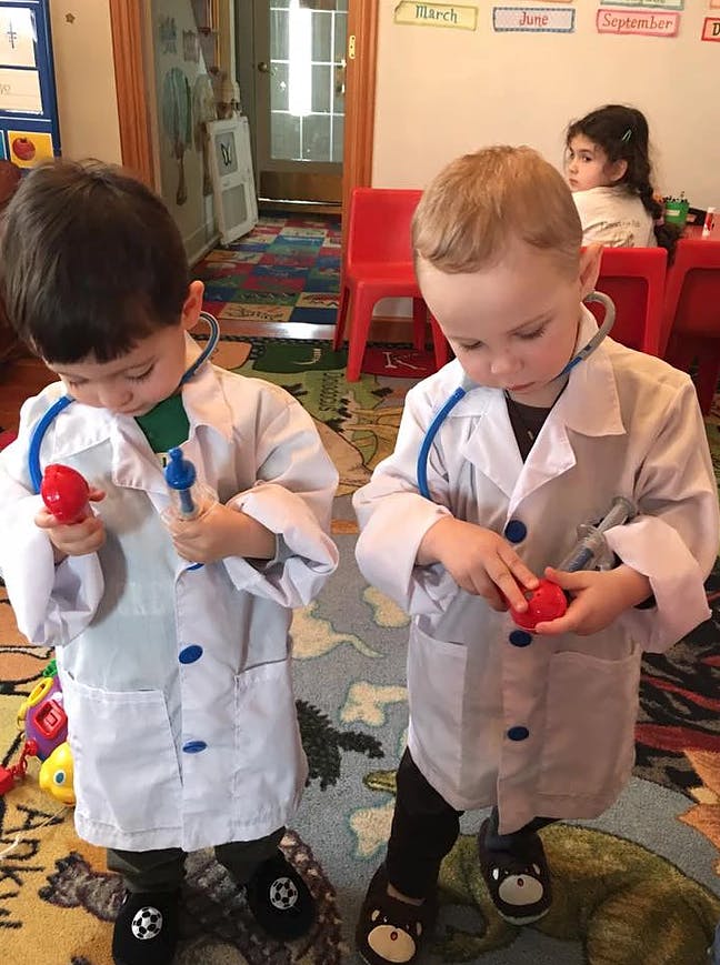 Two children in doctor costumes playing with toy medical instruments