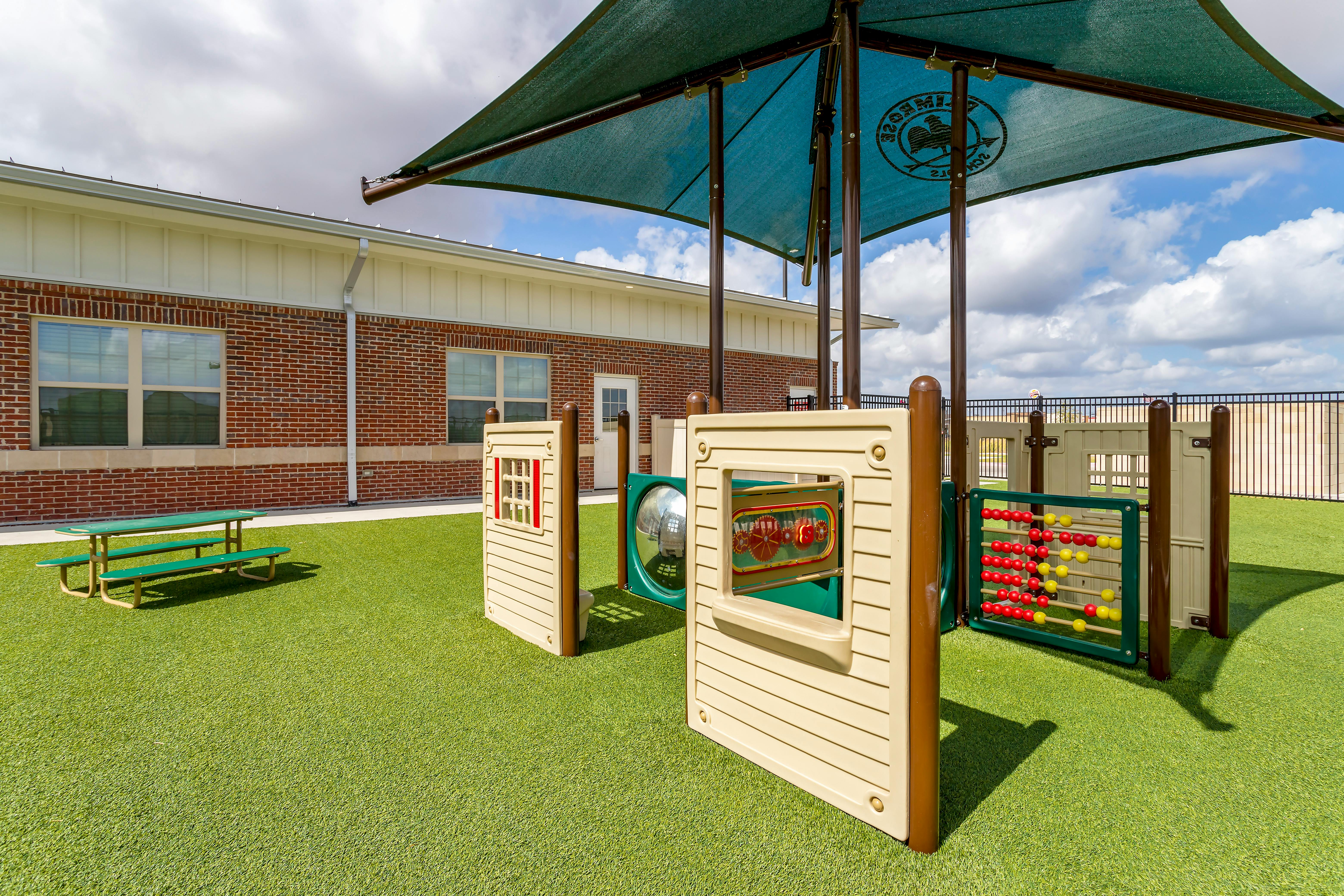 Playground equipment under a teal canopy on artificial grass